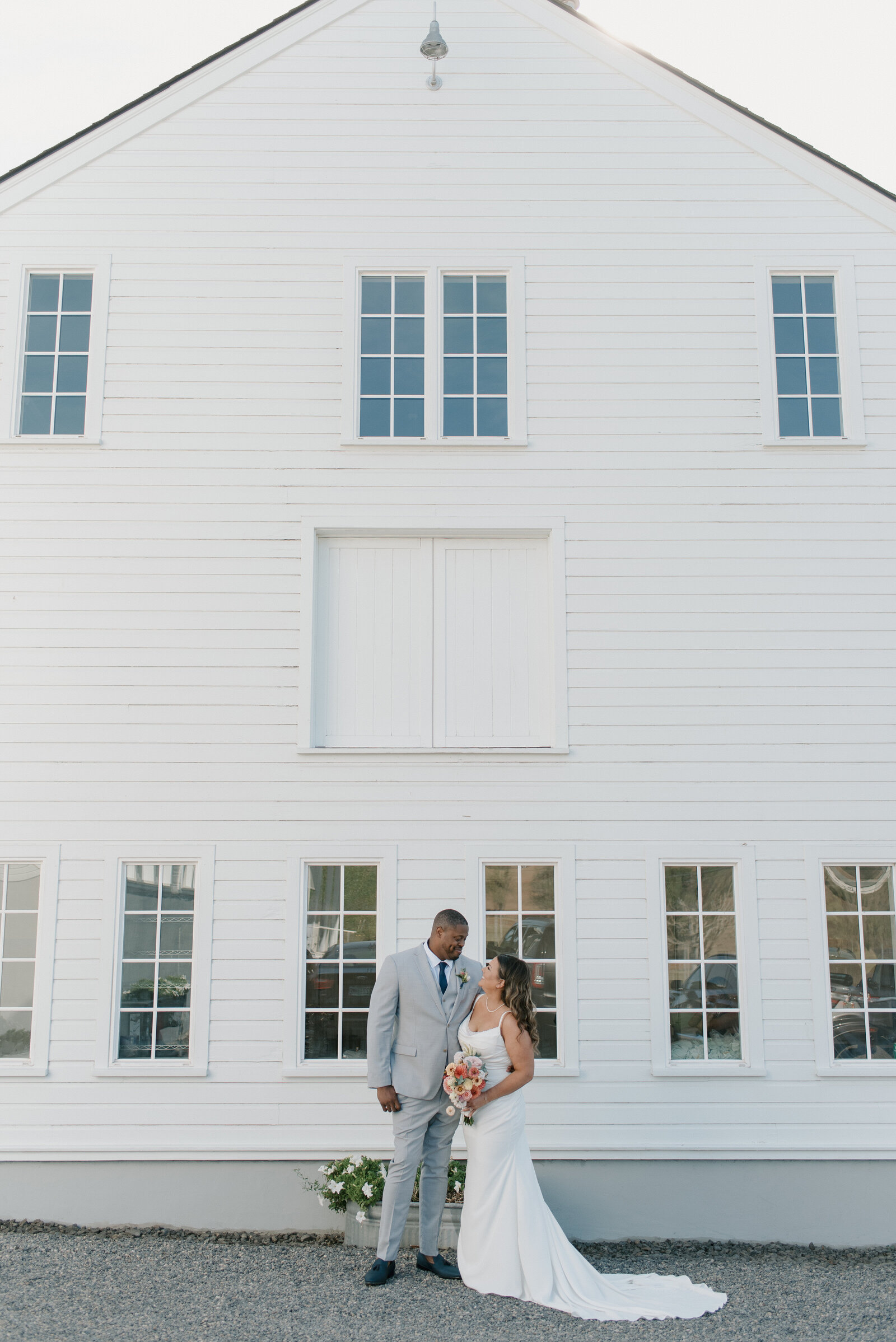 bride and groom of color in front of a white barn at an oregon winery
