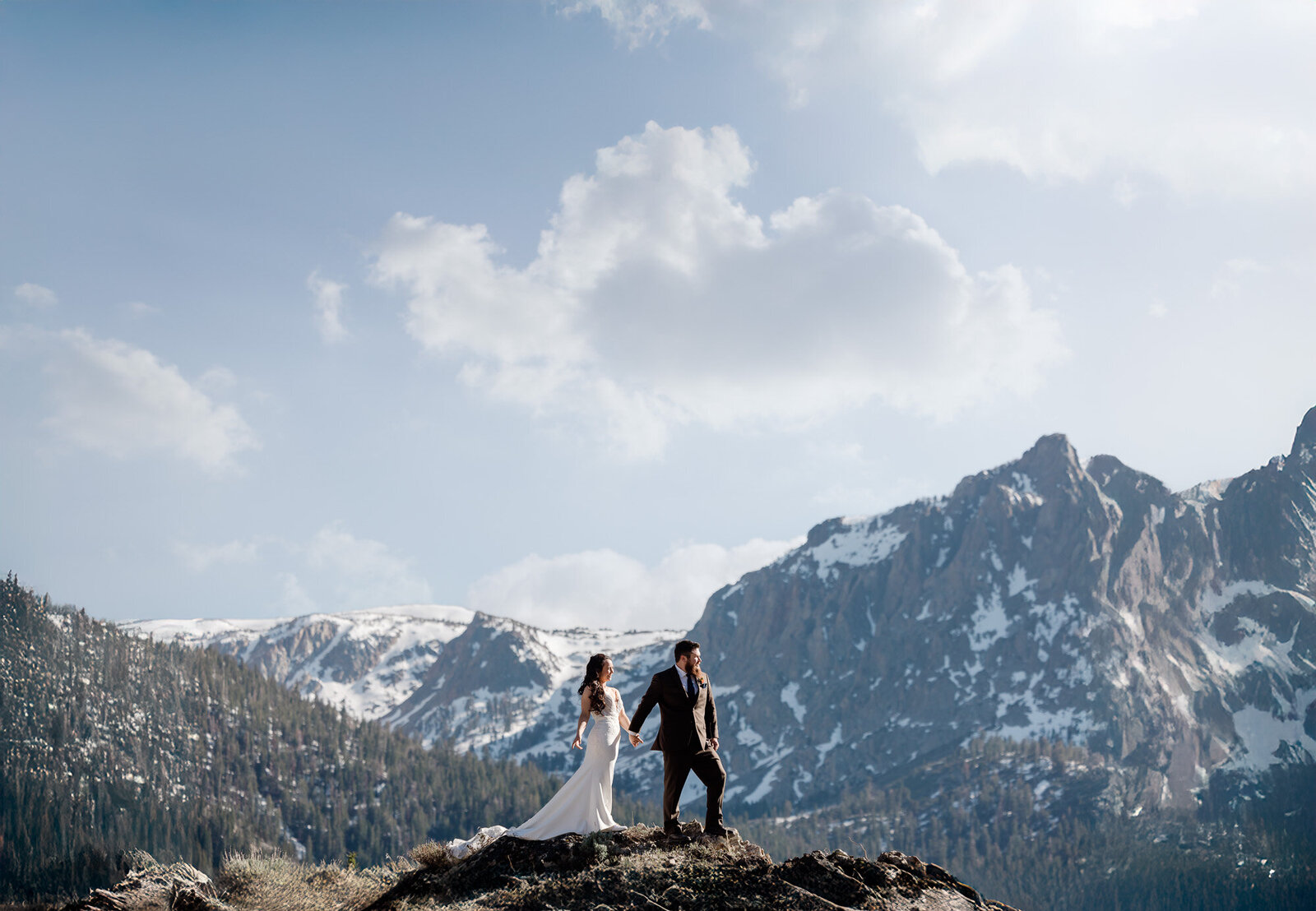 A bride and groom stand in front of snow capped meadows on their sunny Mammoth Wedding day.
