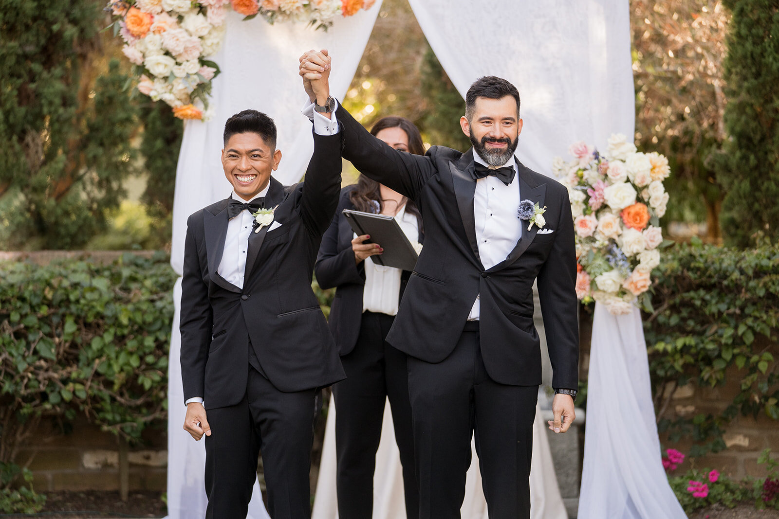 Groom and groom holding hands in the air and facing their guests after being announced they are married