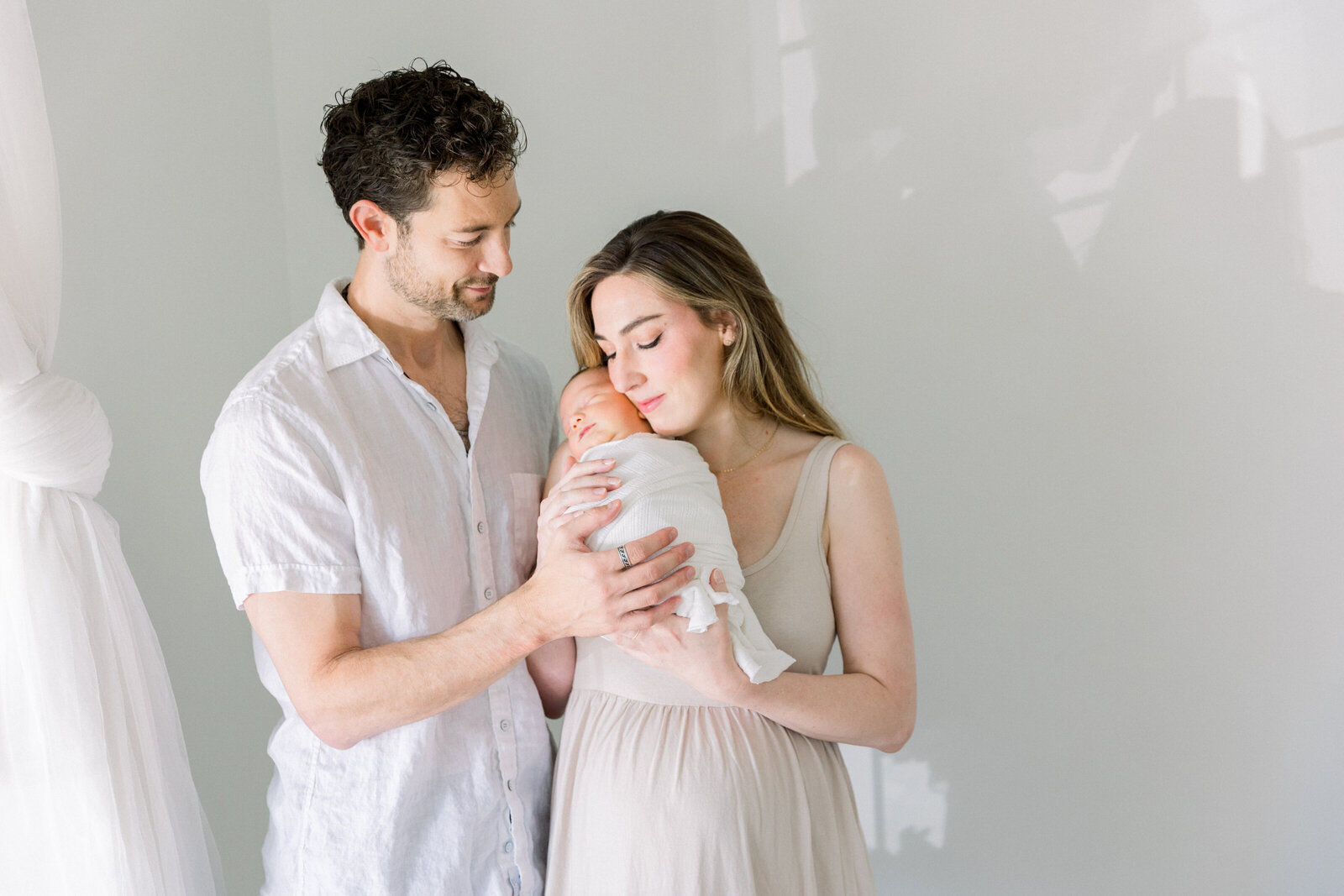 Image of sleeping baby laying on mothers chest with father close by in studio, taken by Newborn Photographer Sacramento Kelsey Krall