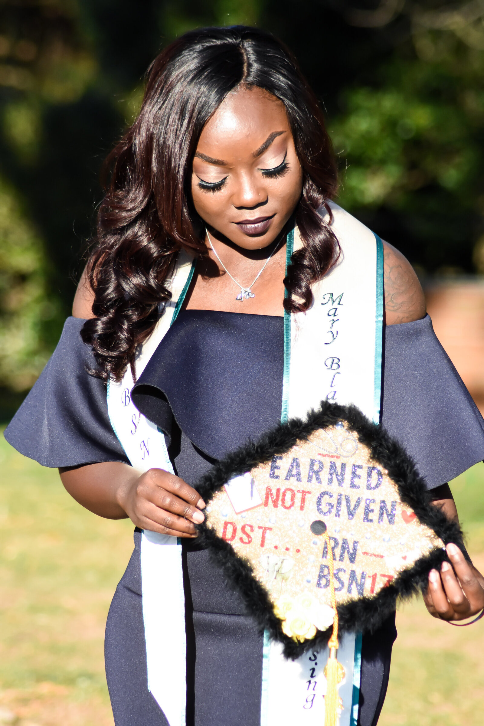 a graduate wearing her green and white stole holding a custom graduation cap that reads "earned, not given. DST, RN, BSN". photographed by Millz Photography in Greenville, SC