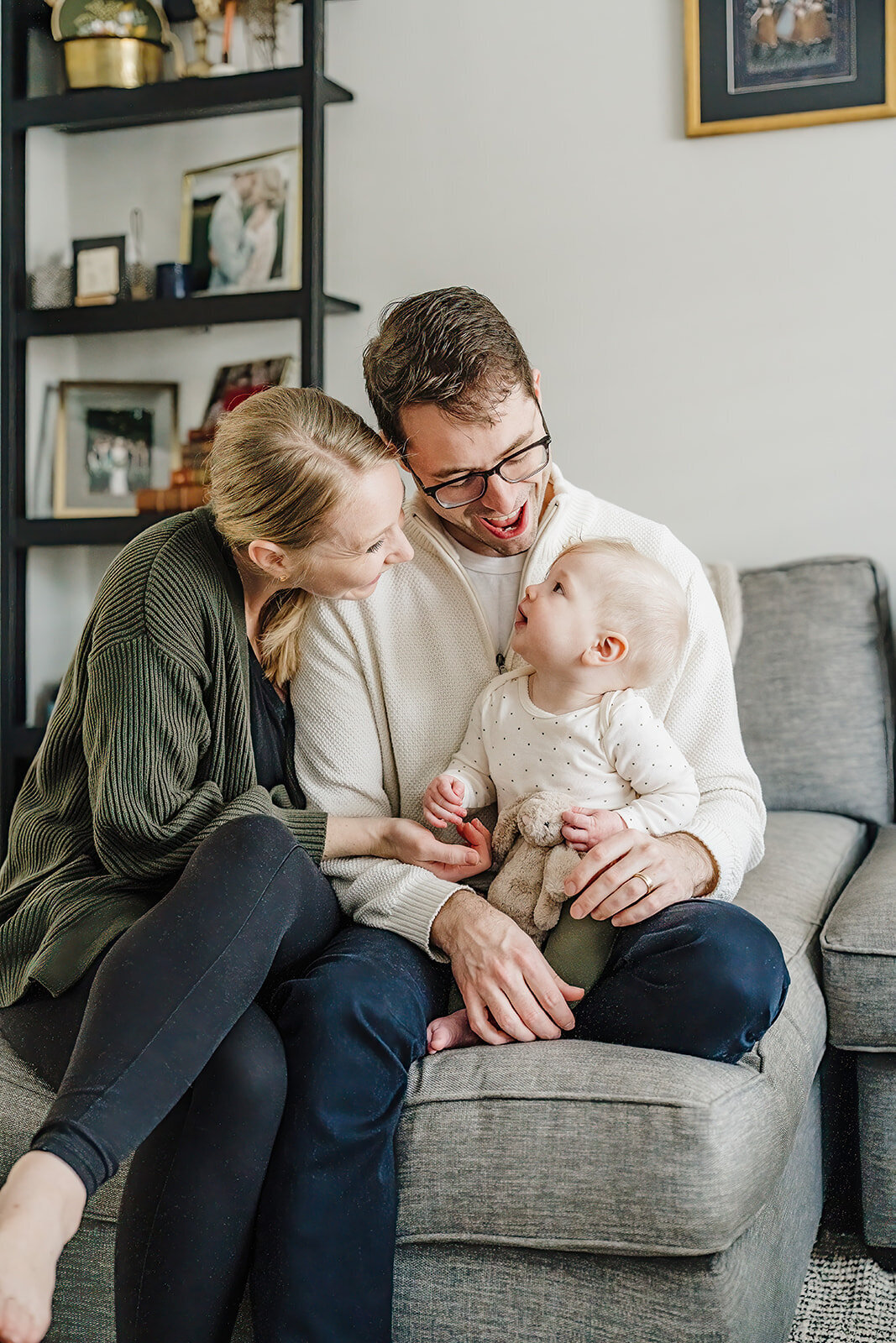 six month old baby sits with parents on couch during sitter session