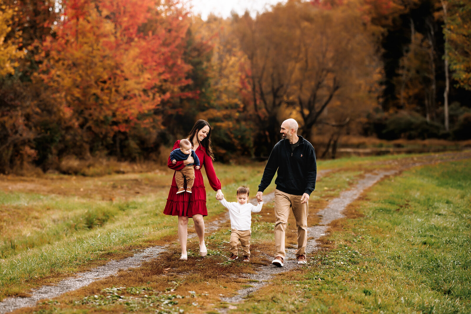 Holding hands, a family of 4 take a stroll along a path lined with gorgeous fall foliage