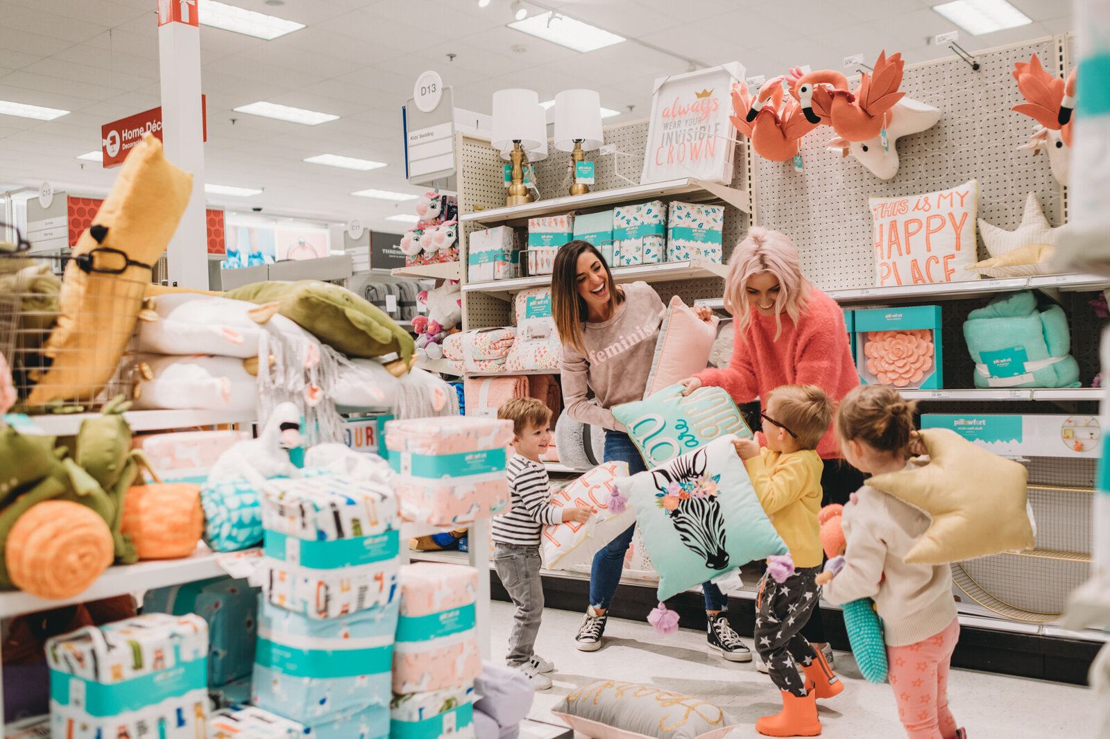 Branding Photographer, a woman with three young children are in a store, they all hold throw pillows and smile