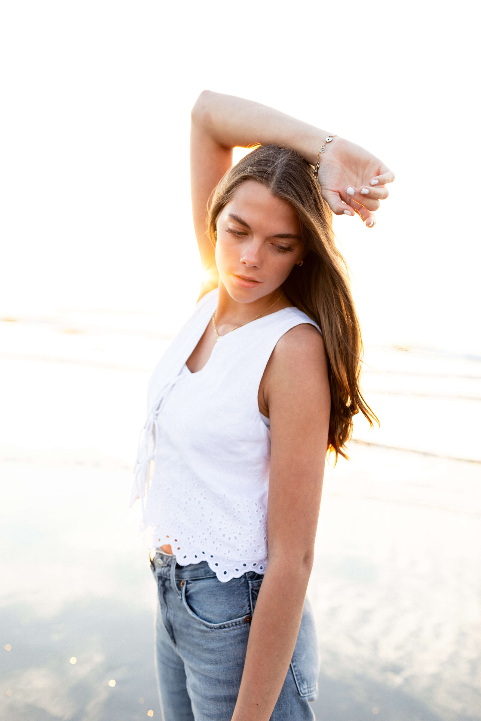 brunette high schooler posing on a beach wearing a white shirt