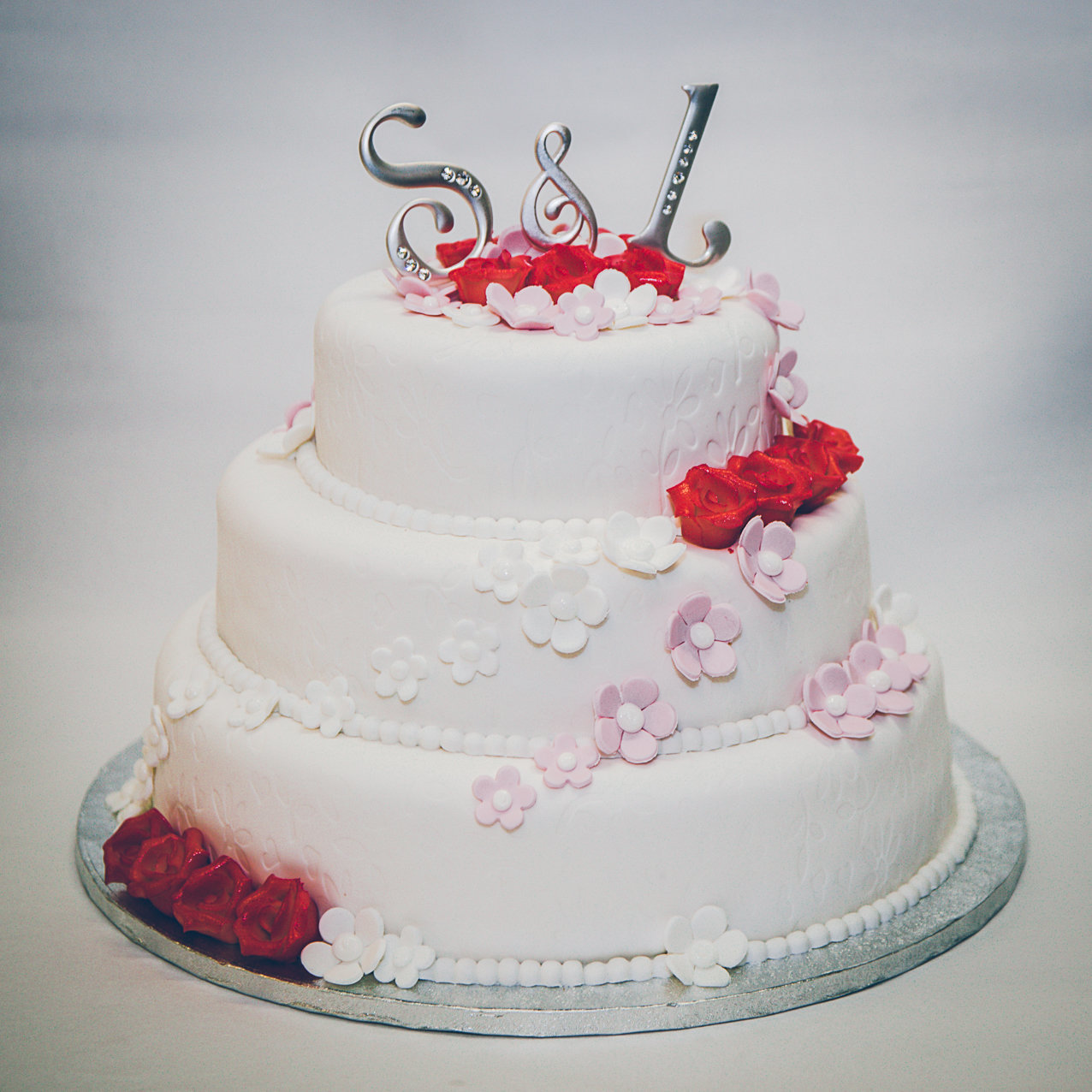 Witte bruidstaart met rode en roze bloemen van Banketbakkerij van den Berg