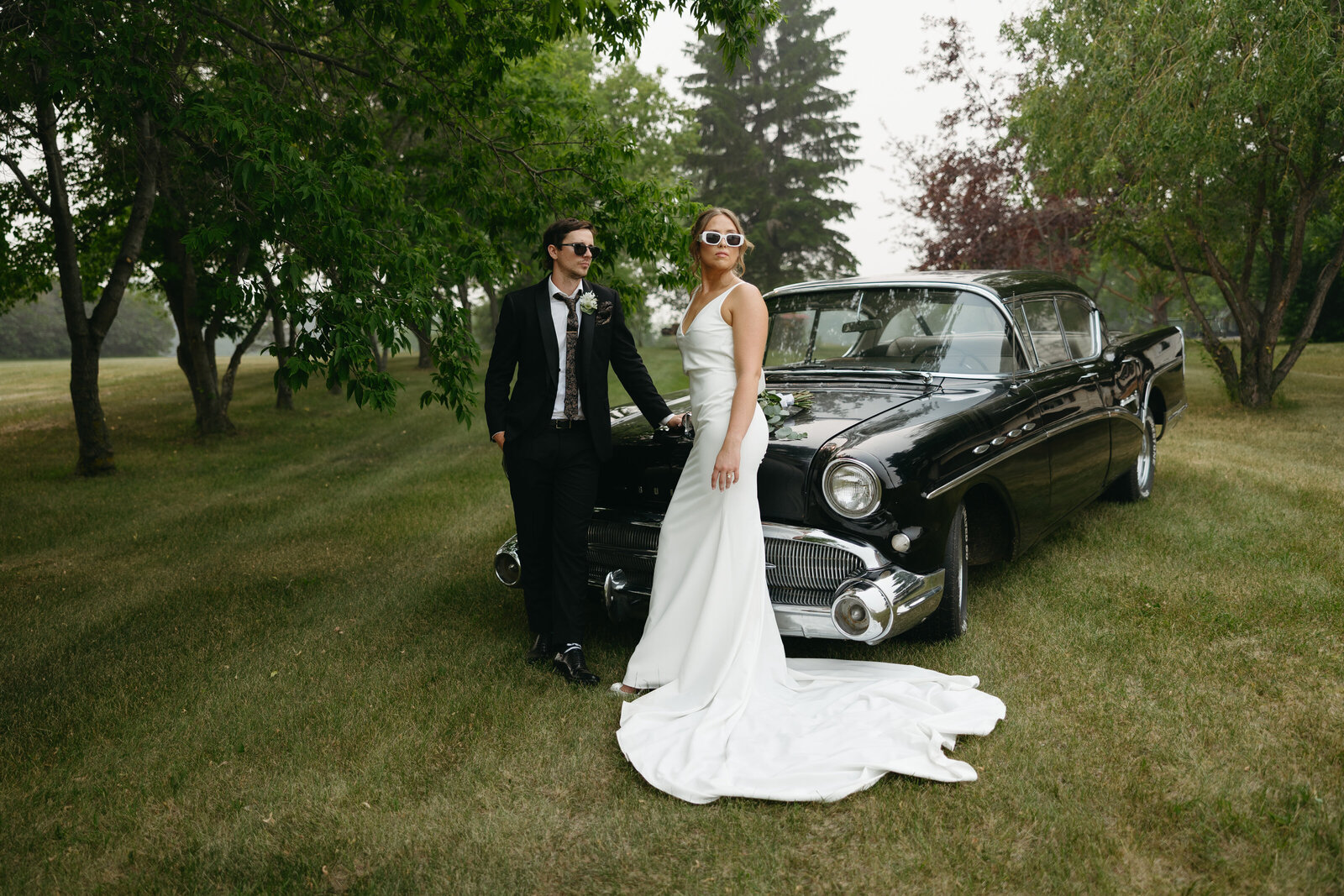 A wedding couple poses with a black vintage car for their wedding portrait after getting married in Nova Scotia. 