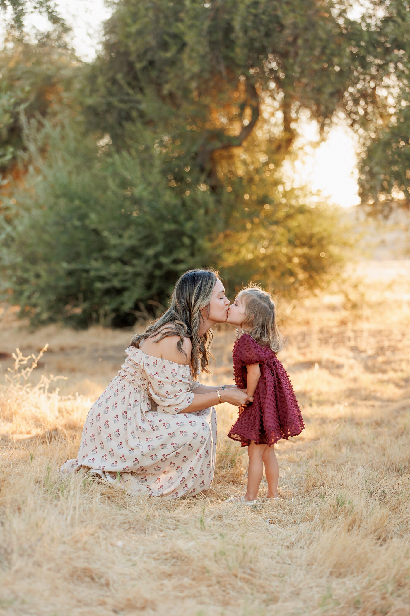 mother and daughter kissing in a field with olive trees, motherhood, fresno, clovis, california photographer