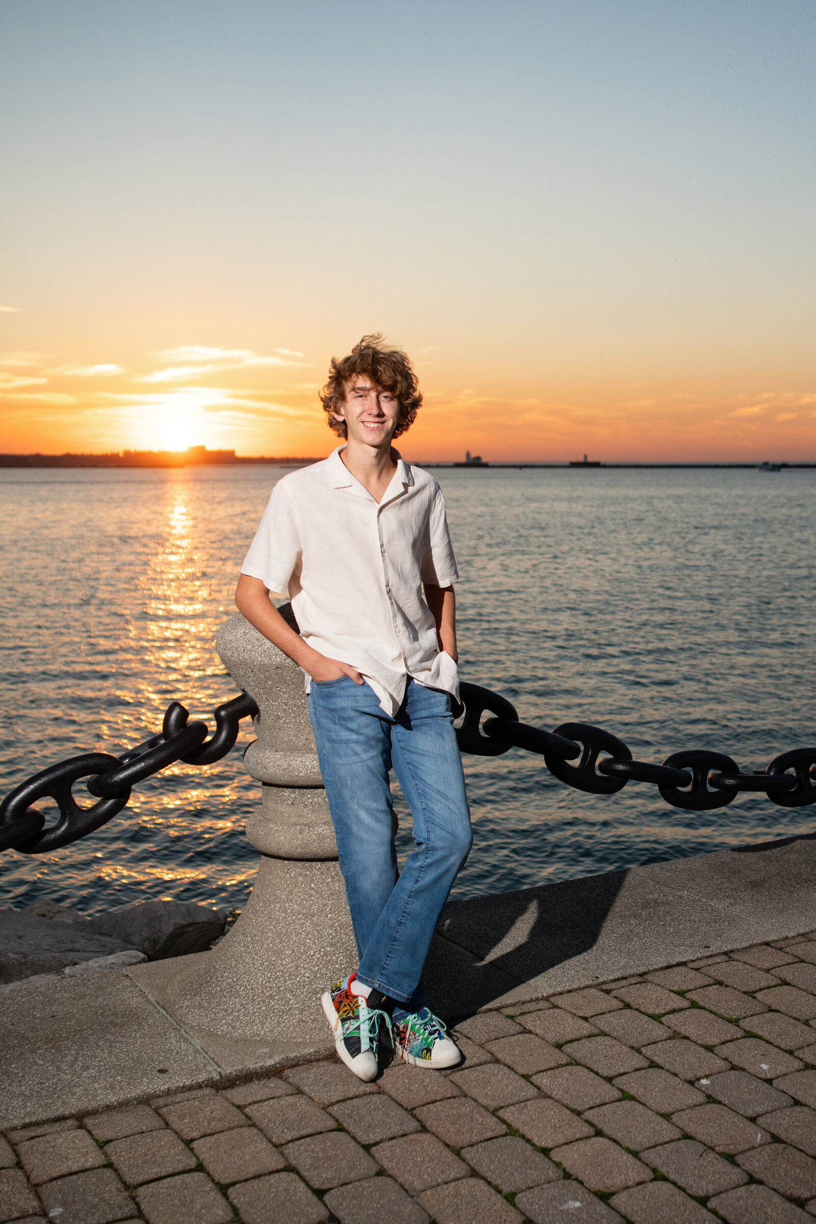 teenage boy leans by chain fence surrounding Lake Erie at sunset