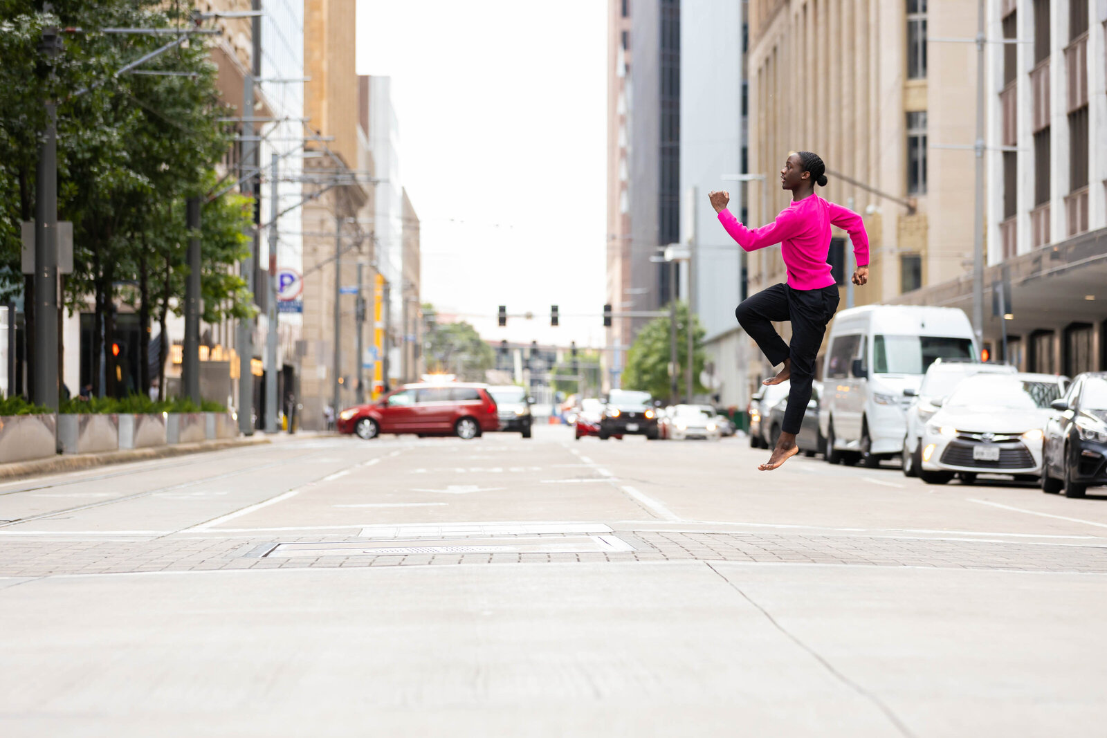 Black male dancer leaping barefoot across city street