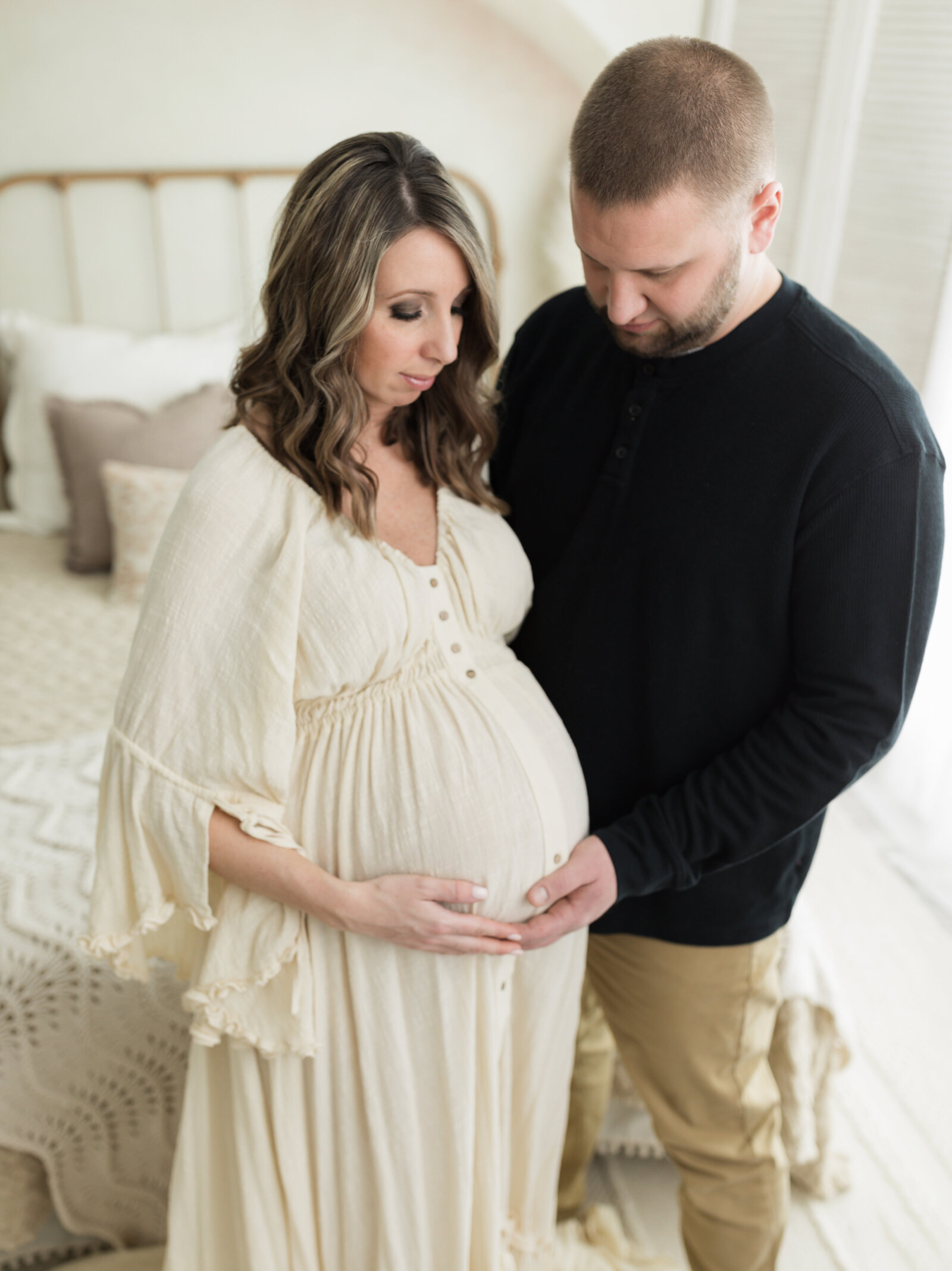 husband and pregnant wife in cream maternity gown holding baby bump for maternity photoshoot