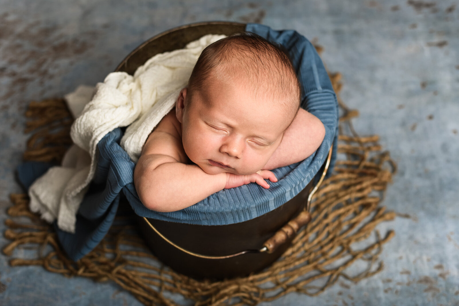 newborn baby laying in bucket with blue blanket for photoshoot