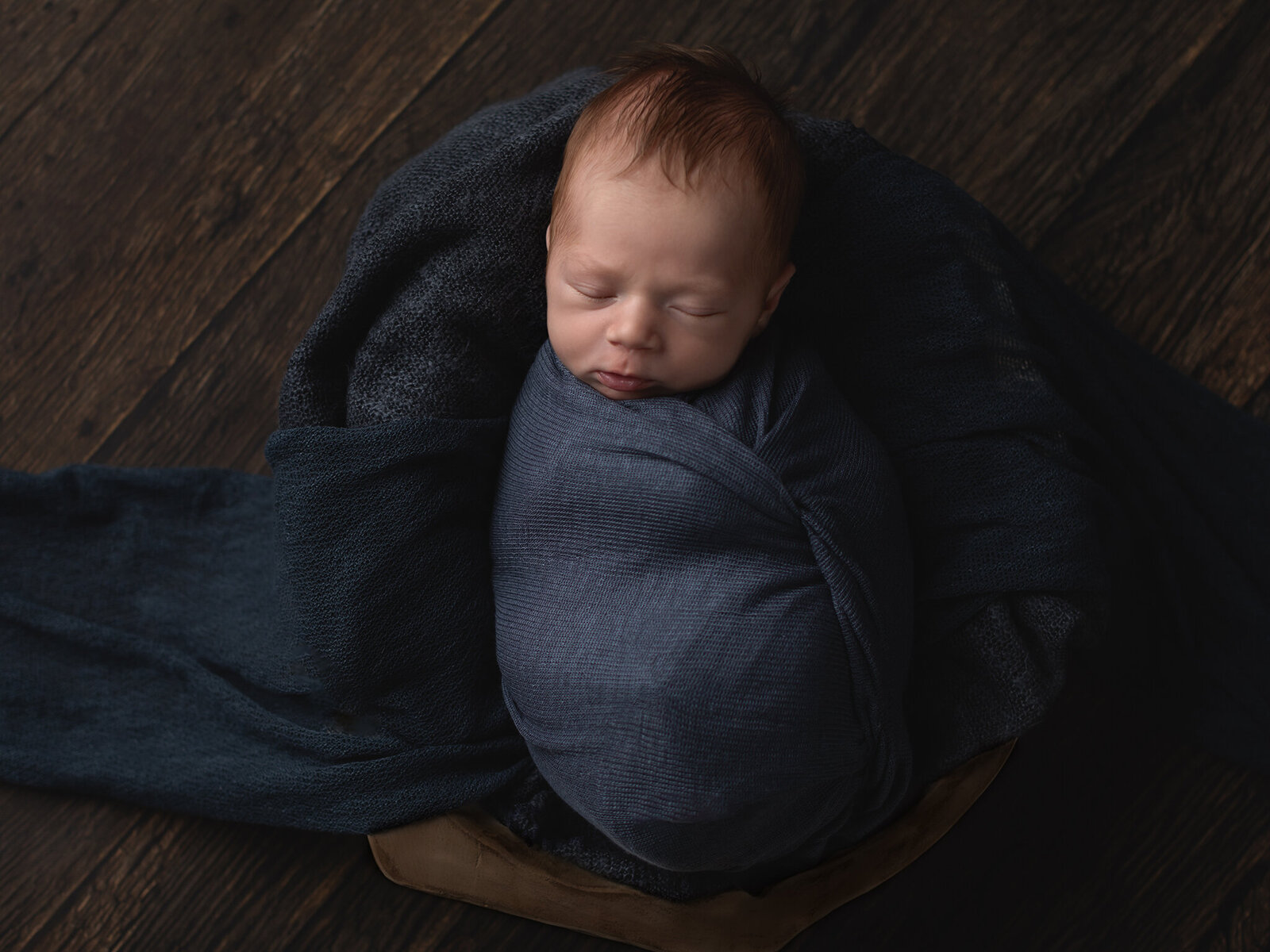 newborn baby boy wrapped in blue swaddle for studio portraits
