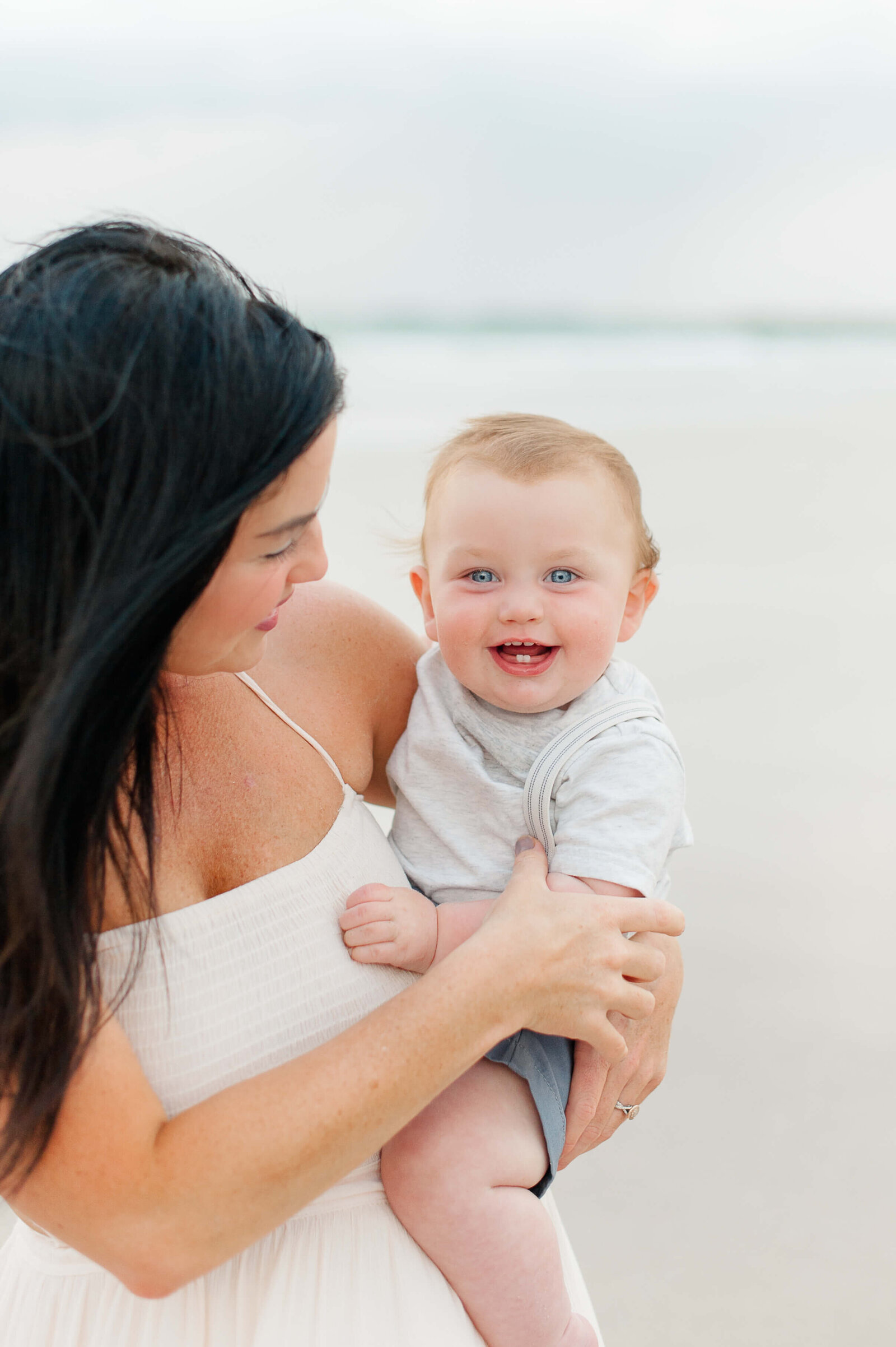 Mom holding a young boy standing on the beach smiling at sunset