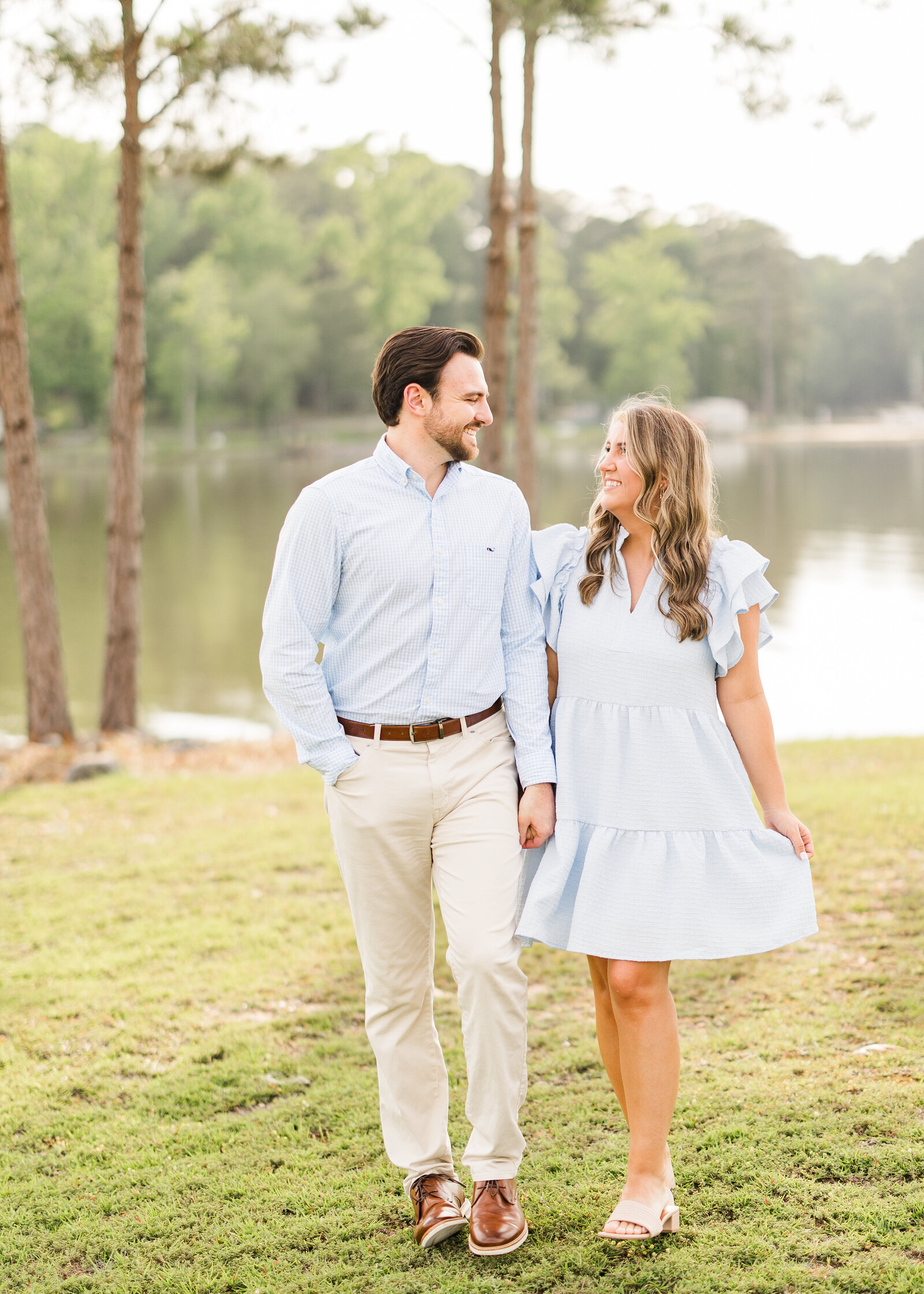 Romantic lakeside engagement photo of Julianna and Josh walking hand in hand, taken by Abby Bell Photography.