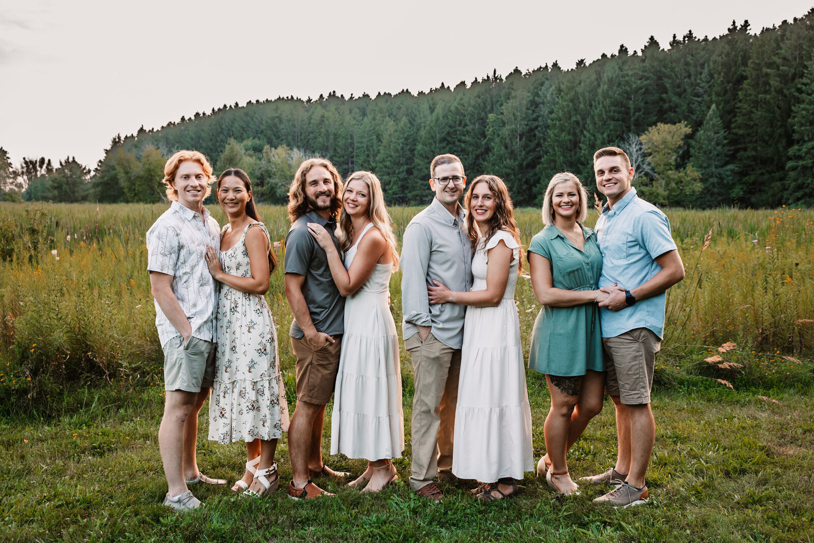 4 couples stand together in a large field at sunset on the edge of tall grasses