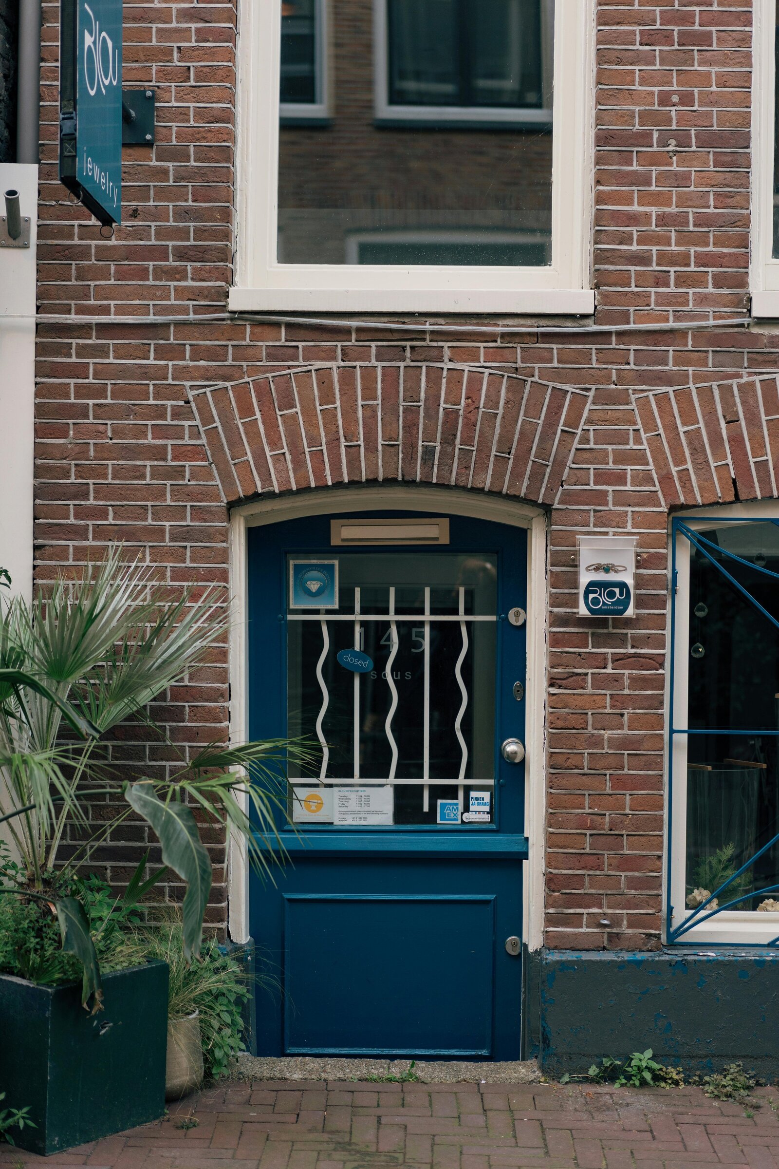 Blue door on a brick building with a window and plants