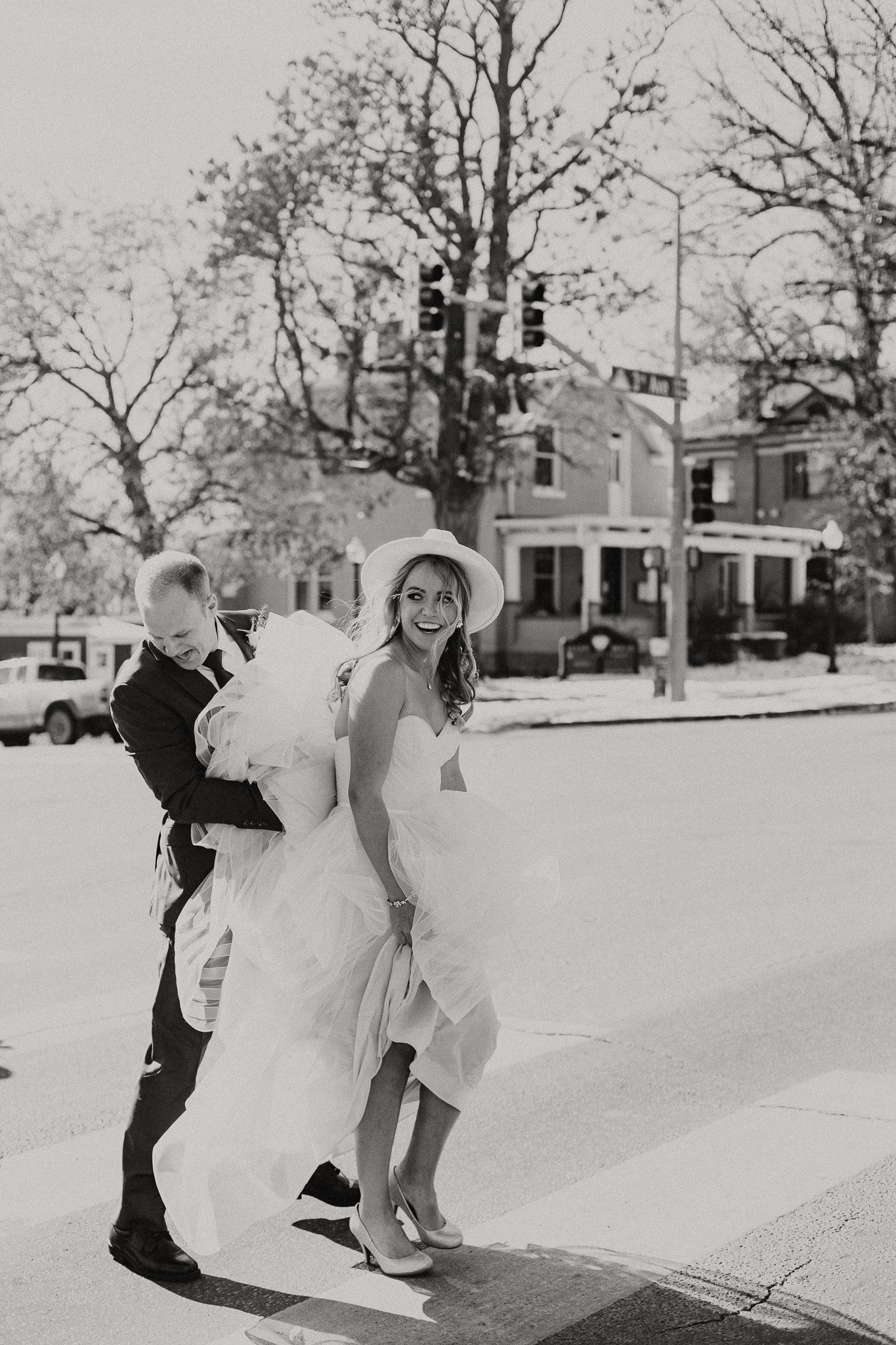 bride walks down longmont street with her dad holding her veil and long train