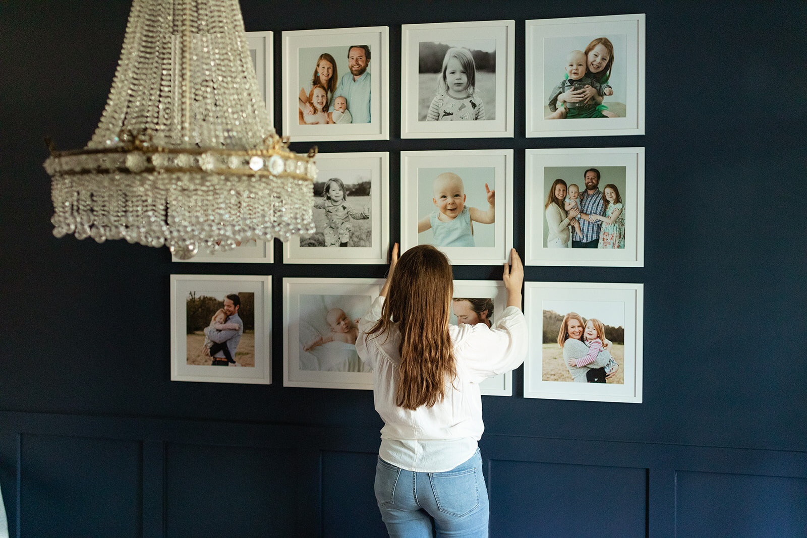 woman hanging family photos in a white frames on a navy wall