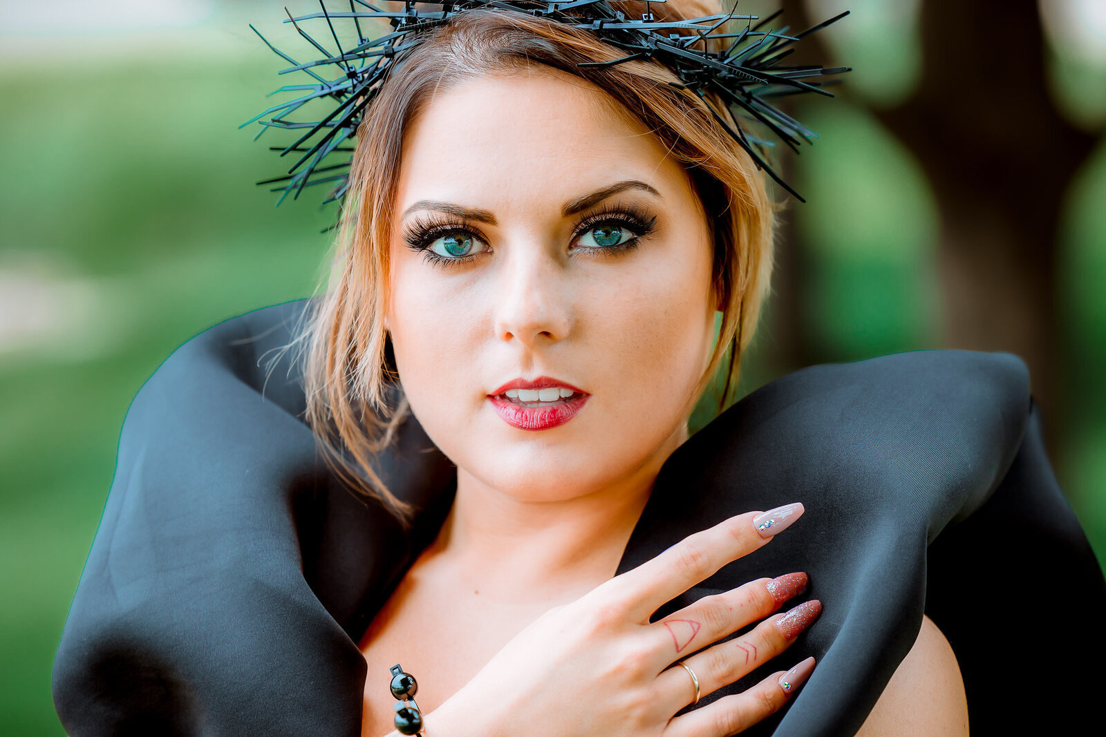 close up of a fairy queen with long nails, black dress, and green background