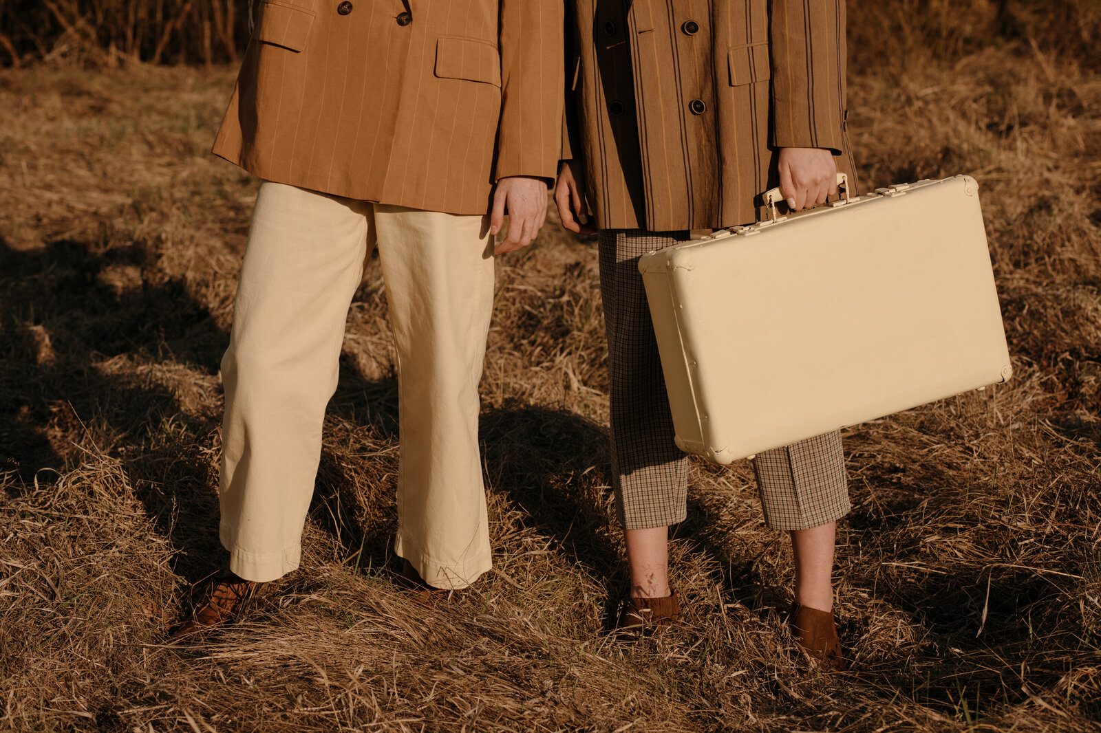 stylish people wearing brown in a field carrying a suitcase