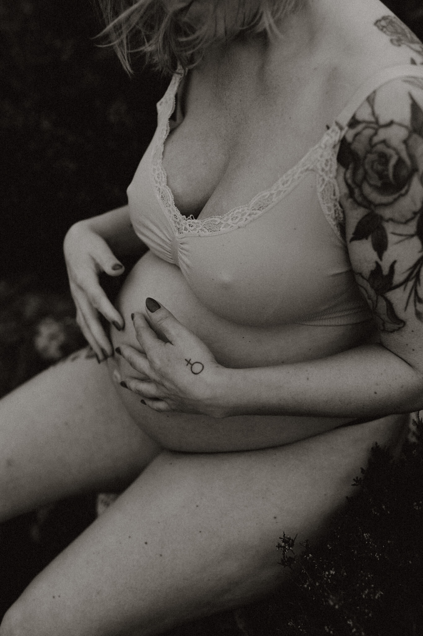 en gravid mamma sitter i underkläder på en sten och klappar sin mage