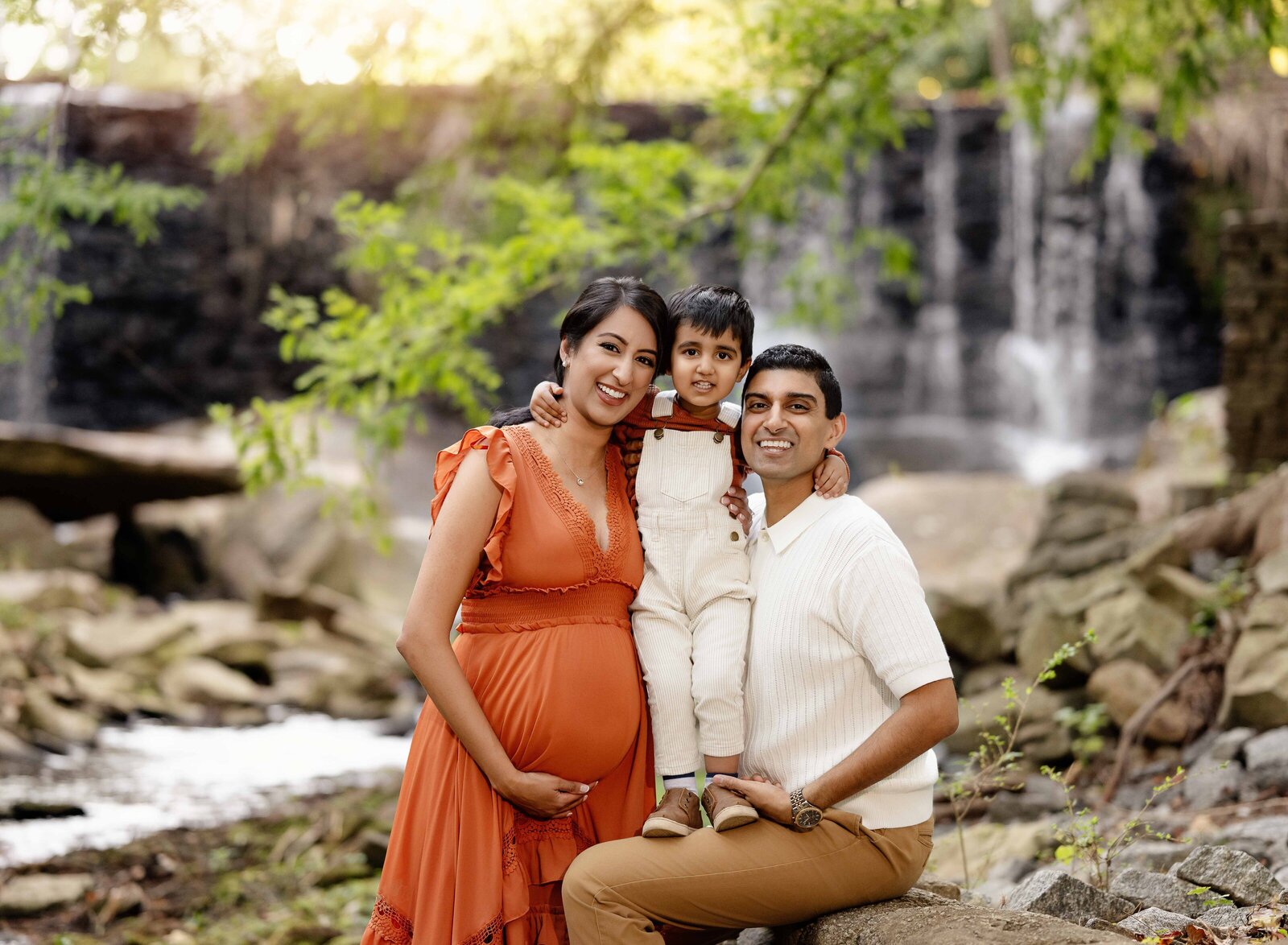 Toddler boy hugging both parents and smiling. Photo taken at a GA waterfall/creek setting near ATlanta.