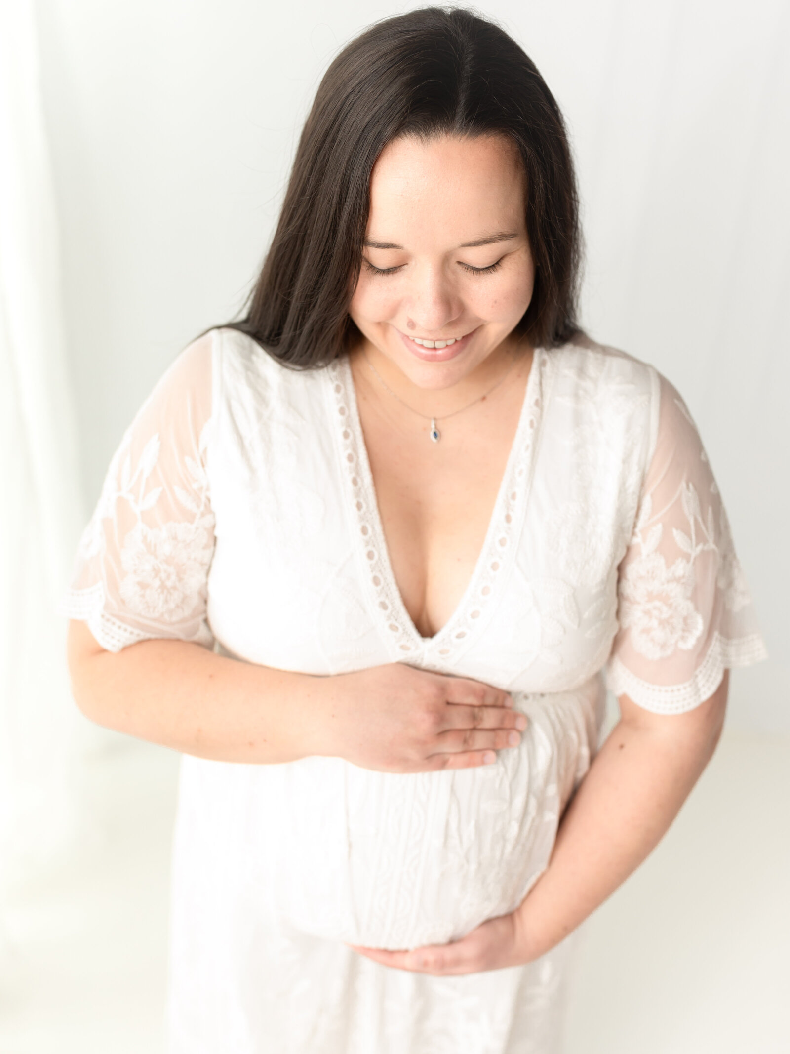 pregnant mother in white lace dress holding belly for maternity photos cleveland maternity photographer