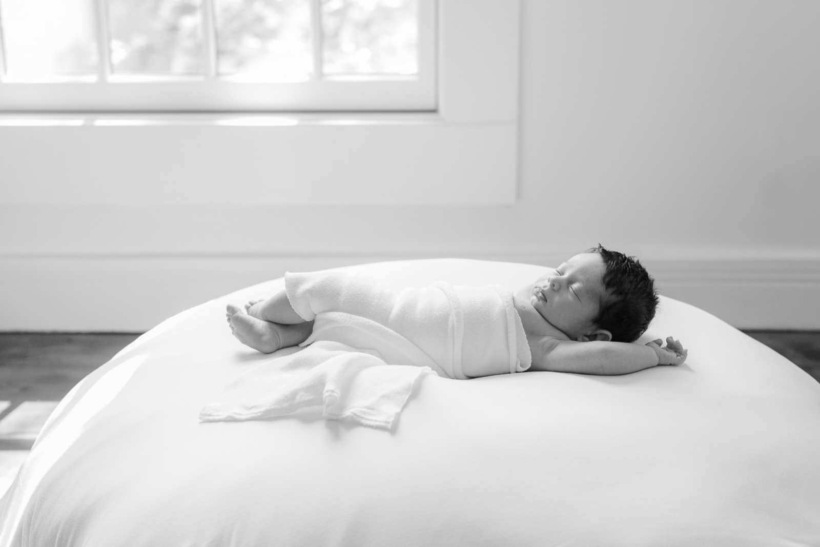 black and white image of newborn baby wrapped in white swaddle sleeping during in home newborn session