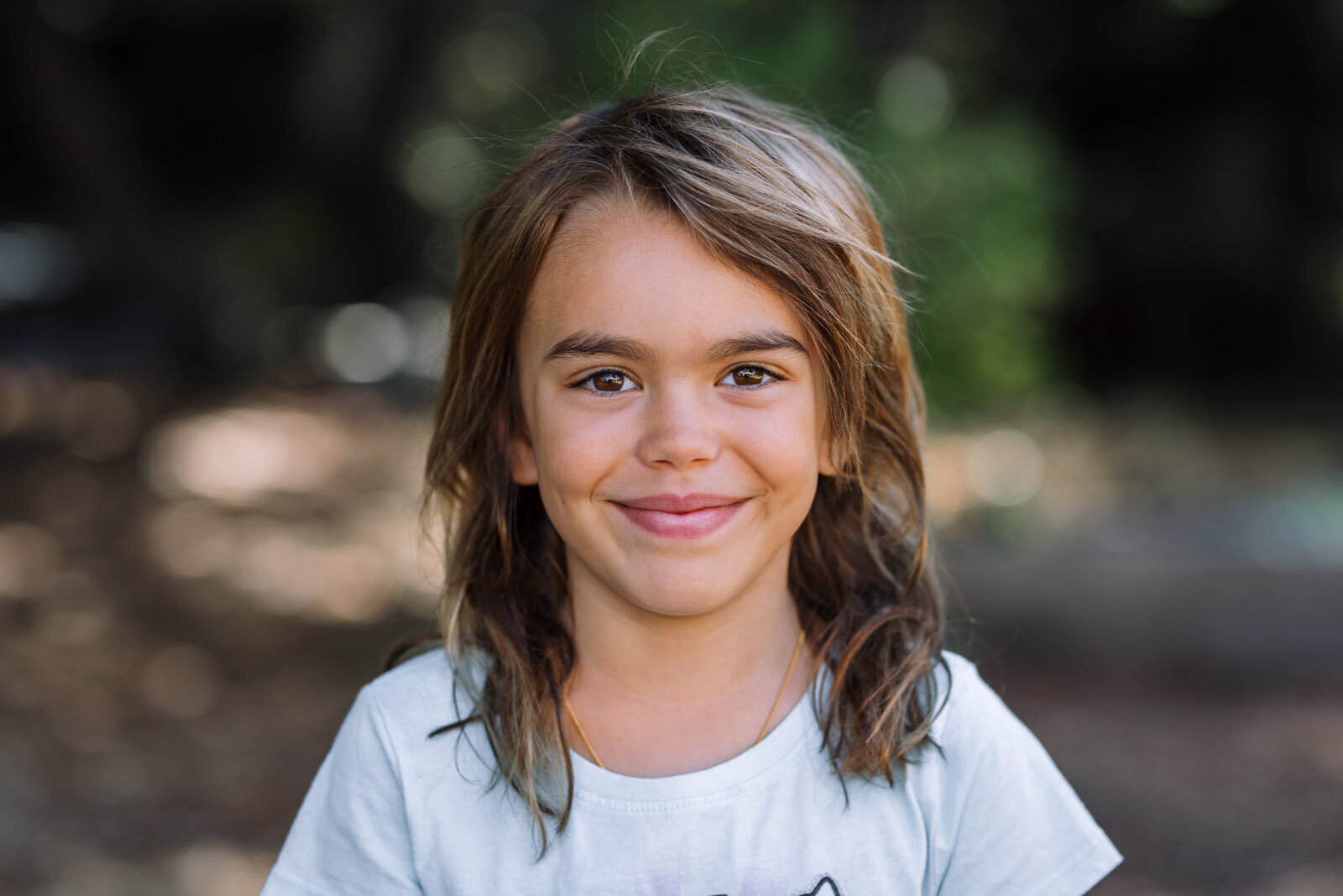 portrait of a 7-year-old girl with long hair looking at the camera and smiling while standing in a school garden