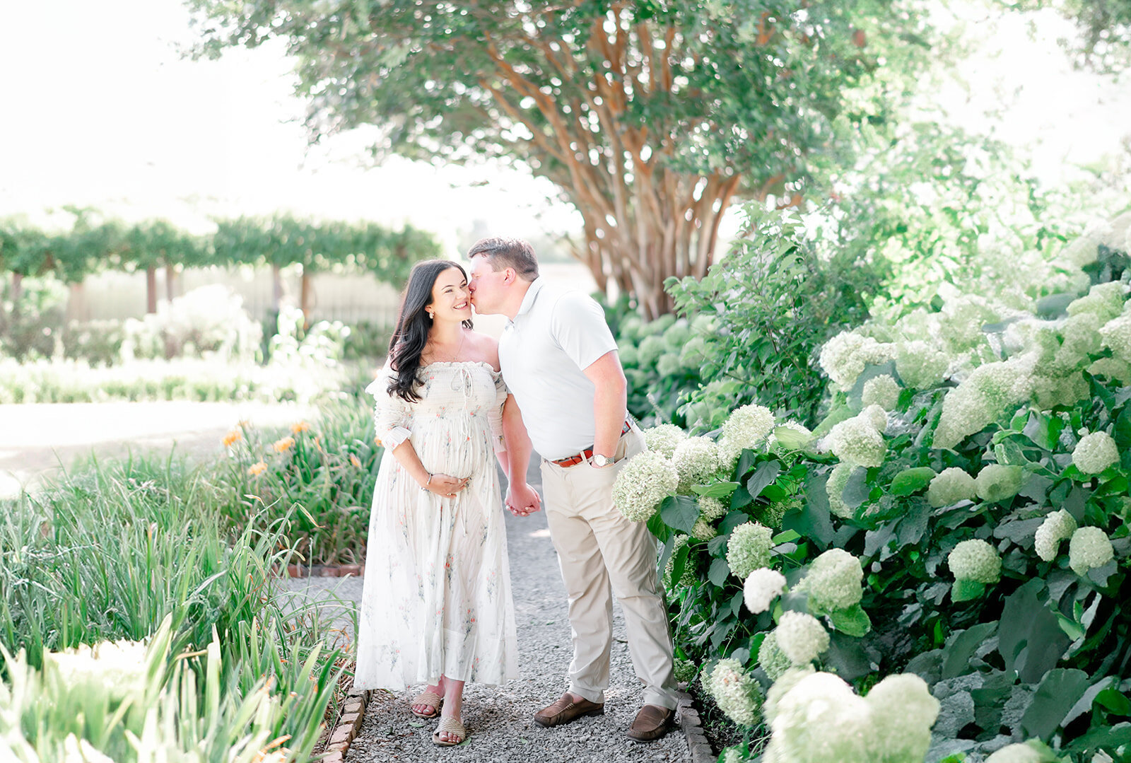 Pregnant couple walks beside white hydrangeas by Nashville maternity photographer Kristie Lloyd