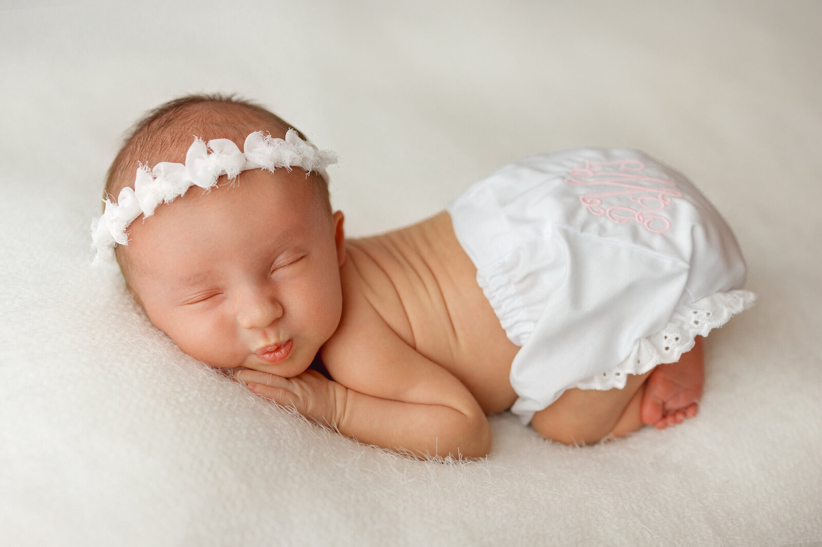 Newborn baby girl wearing heirloom monogramed bloomers posed on white fabric