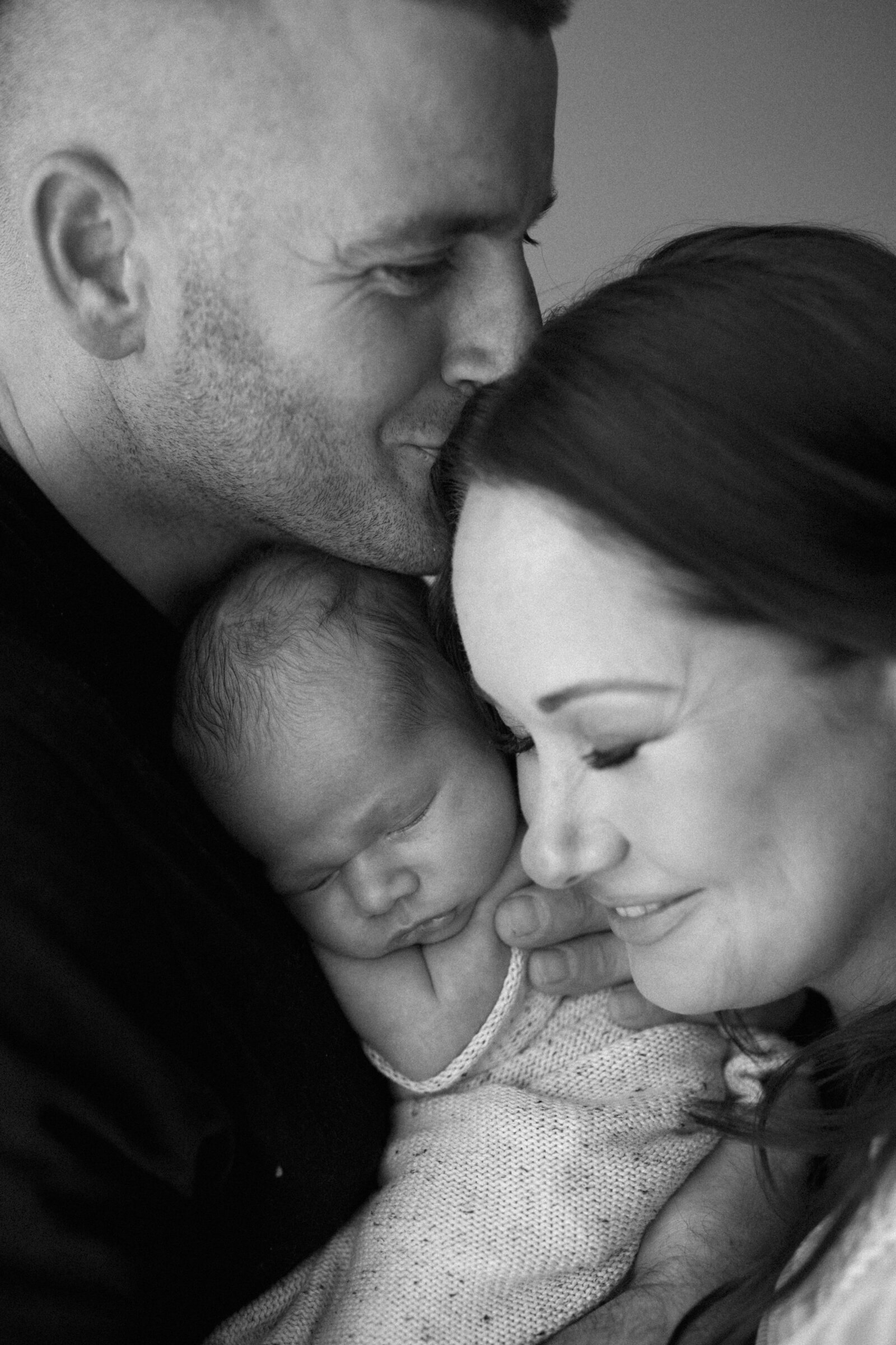 Studio newborn family photography in Perth – a beautiful, intimate portrait of new parents holding their baby in soft natural light.