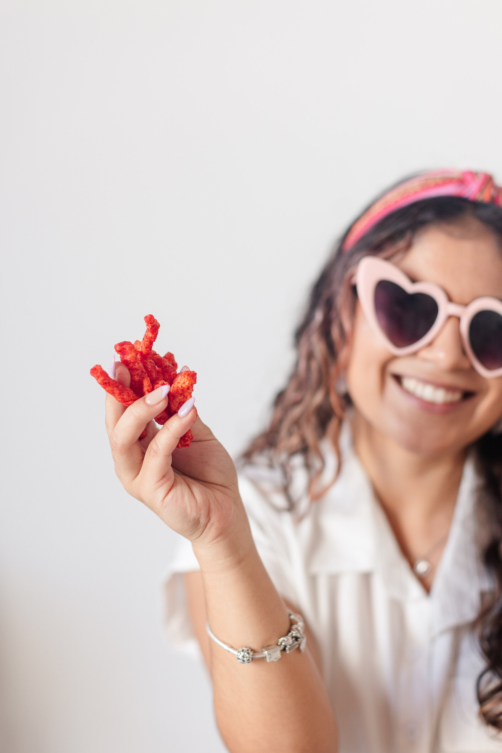 a woman with heart shaped sunglasses holds a handful of flaming hot cheetos in her hand