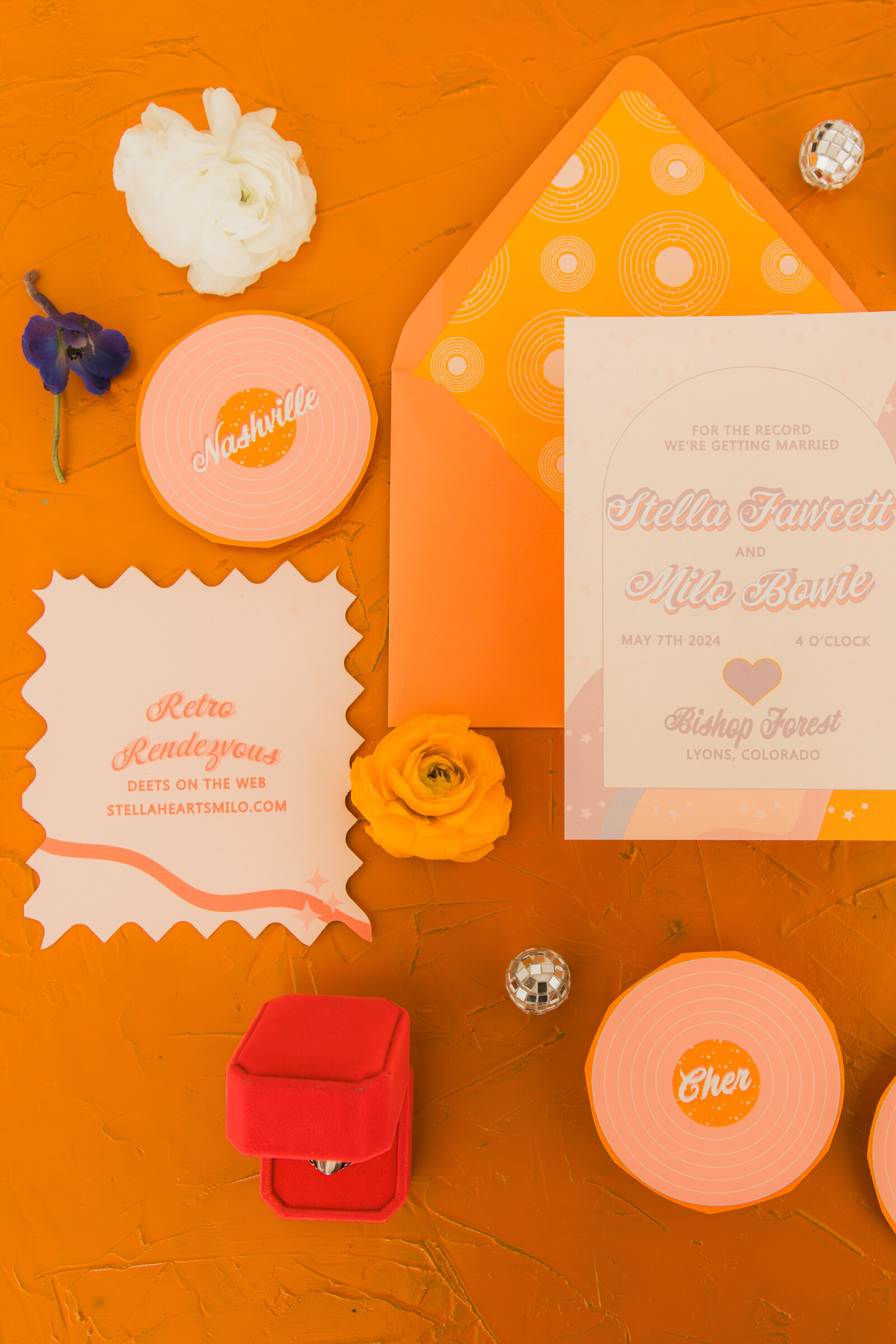 A waxy shaped wedding details crd under a record shaped wedding place card and next to a rinbow wedding invitation.