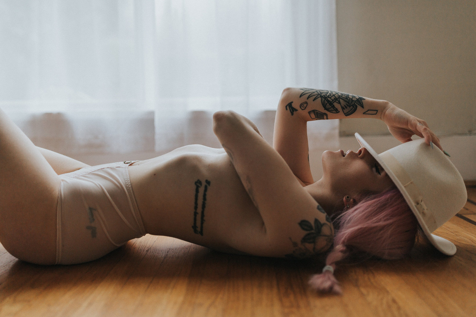 girl lying down on floor topless holding her hat during her boudoir photoshoot