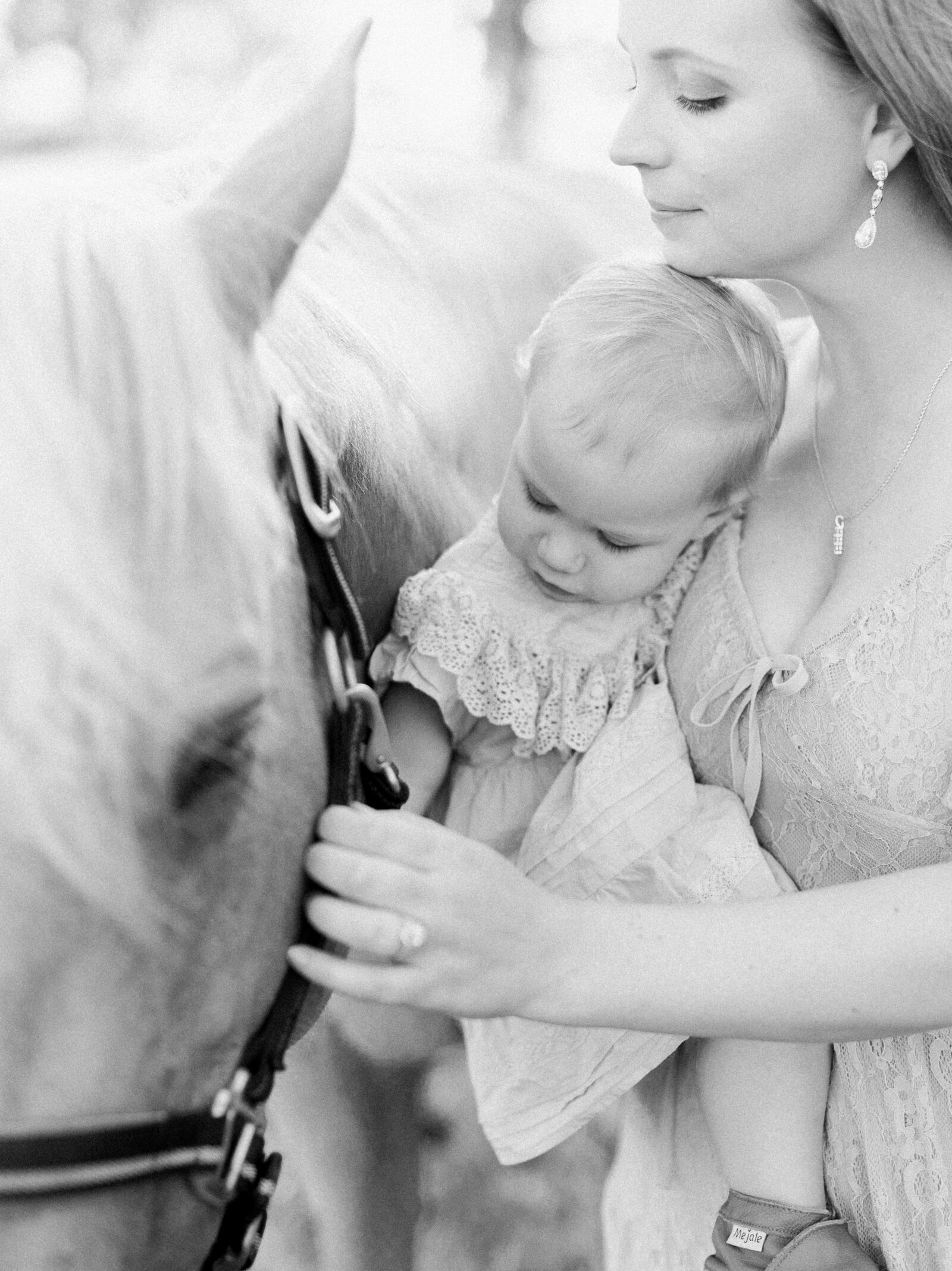 Closeup of mom holding one year old on her hip as she pets their palomino horse on a horse farm by NH newborn photographer Fieldstone Studio.