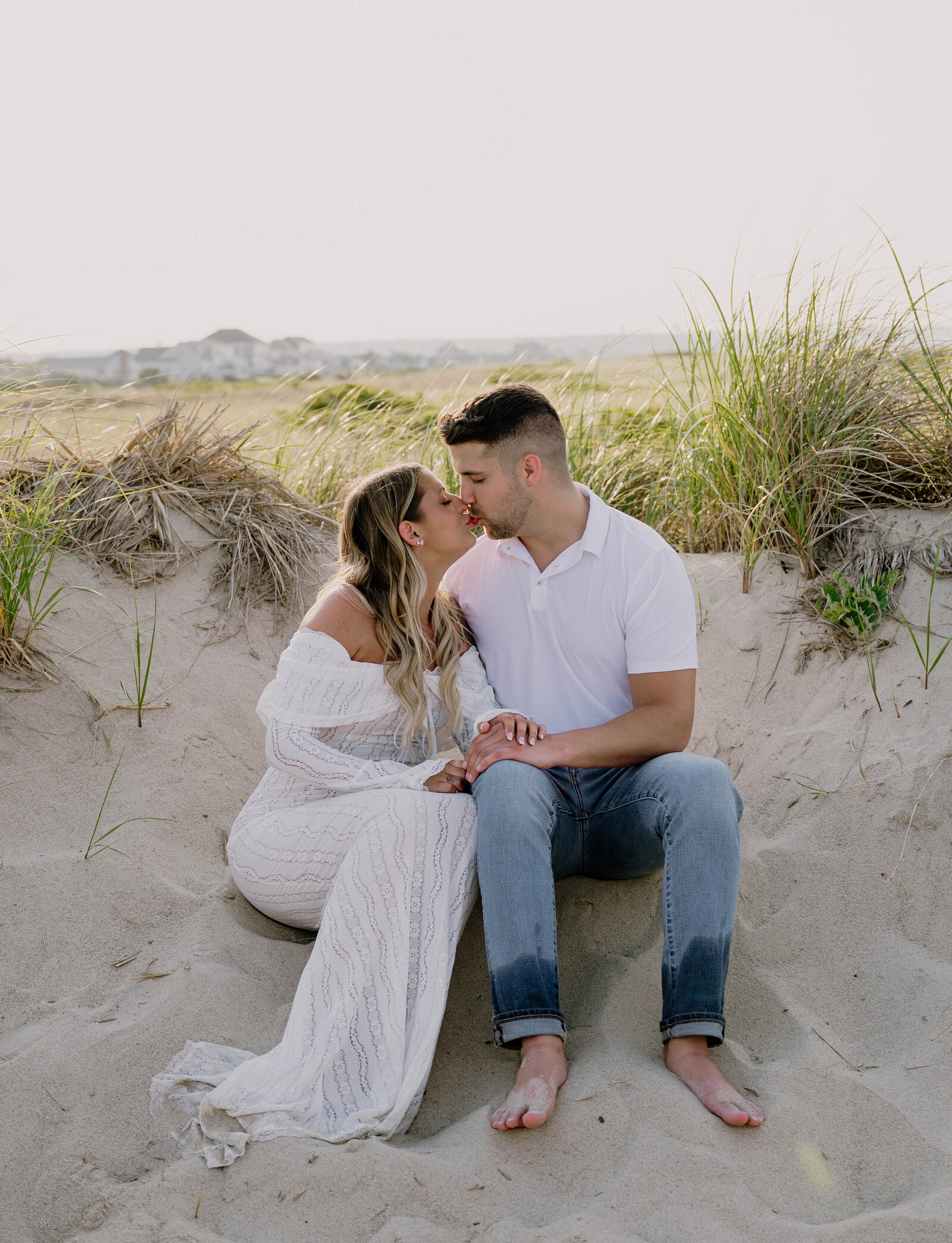 Engaged couple sitting in sand on a beach in Massachusetts