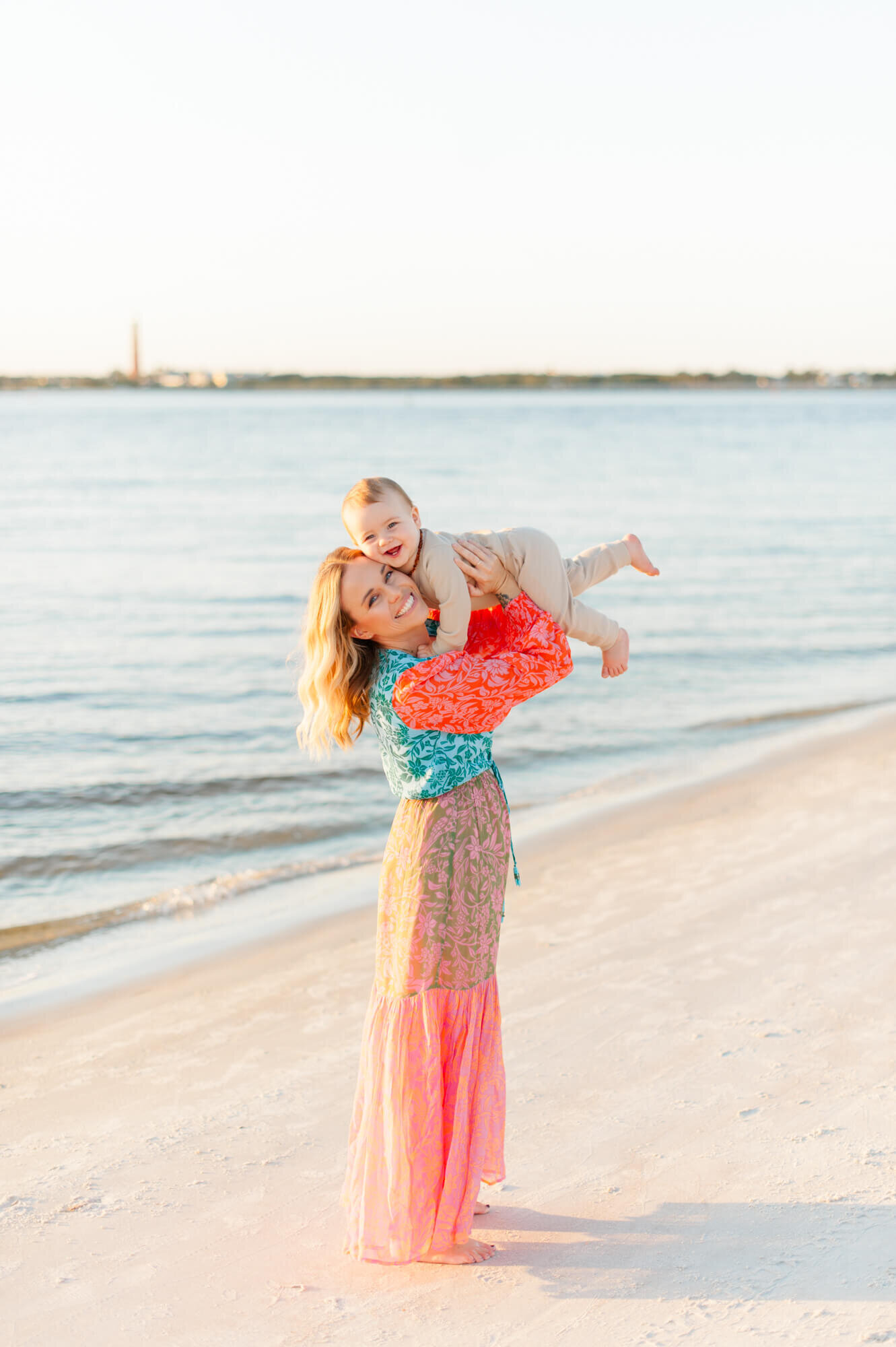 Young mother laughs with her son while holding him in the air near the shoreline on Vero Beach!