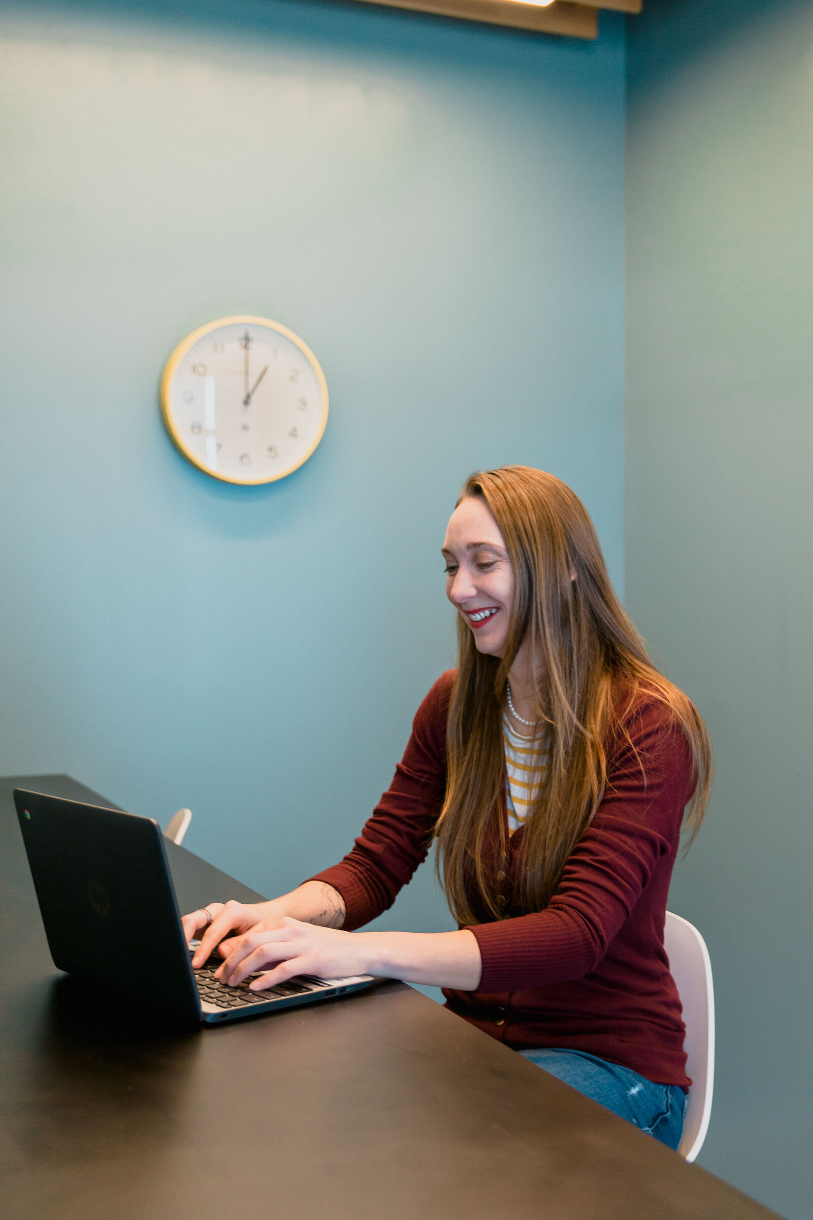 Small business owner typing on a laptop and a coffee shop while smiling for her brand photography