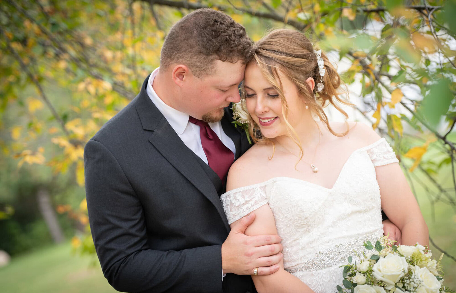 wedding couples snuggles heads together under fall leaves