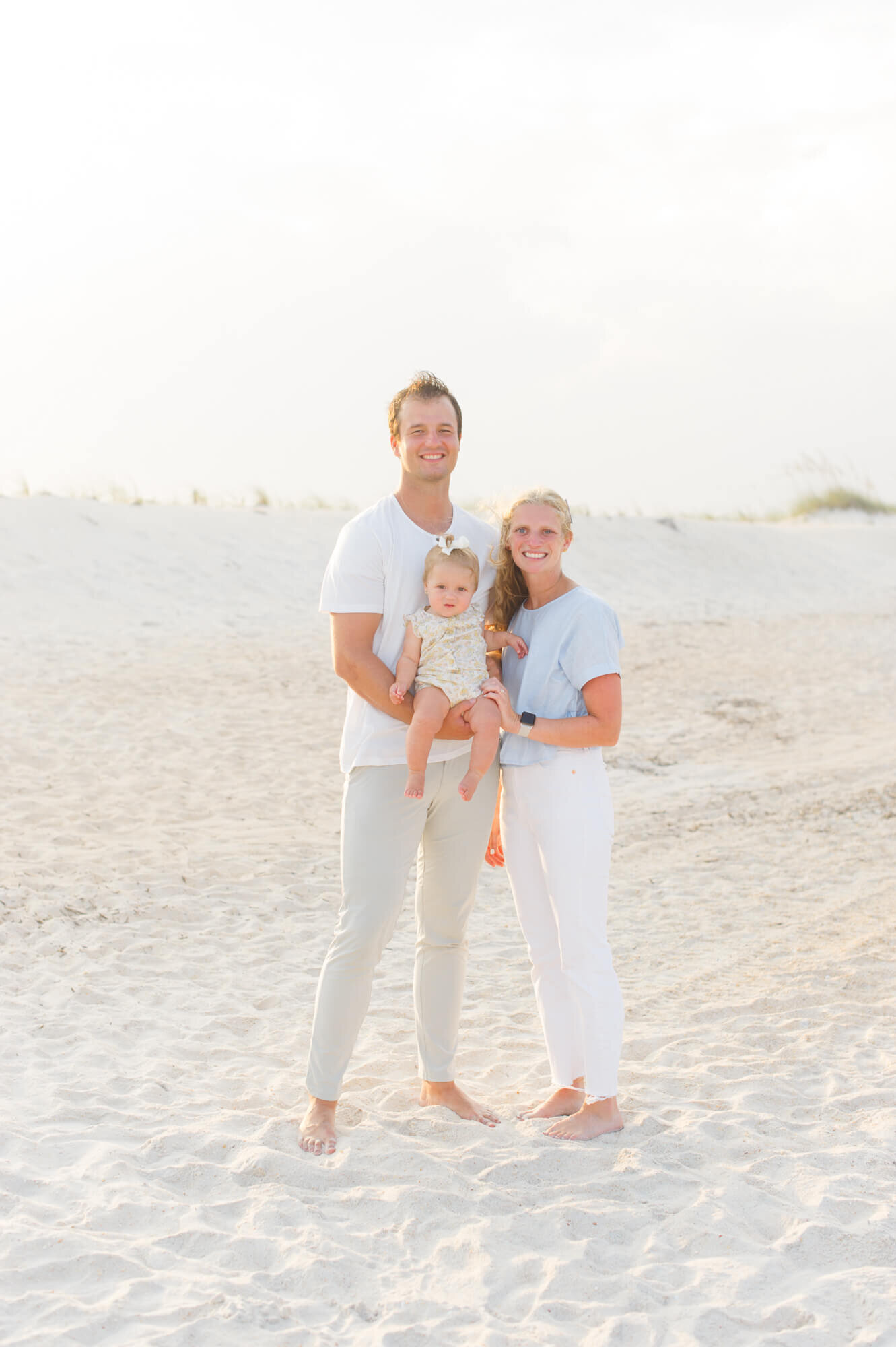 Family of 3 standing in the white sand smiling for a family portrait on Vero Beach