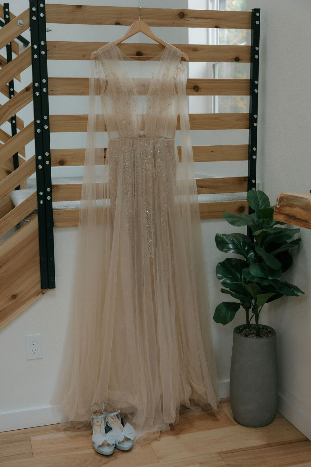 Flowing blush wedding gown hanging beside a wooden staircase
