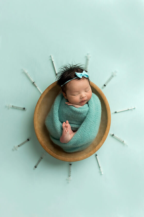 Newborn girl sleeps in a bowl with all the needles from her IVF surrounding her.