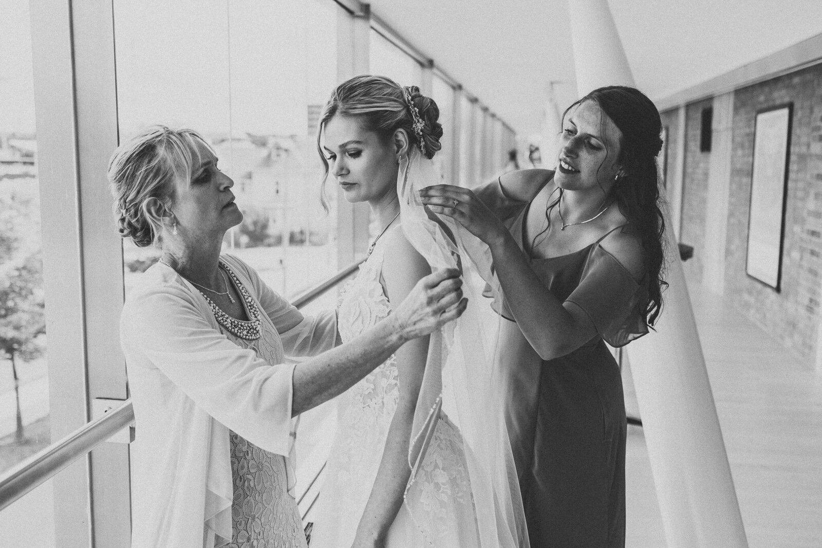 A timeless black and white photo of a bride being assisted with her veil by her mother and maid of honor 