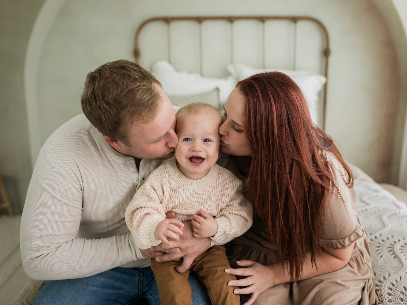 mom and dad kissing their one year old son for family studio portraits 