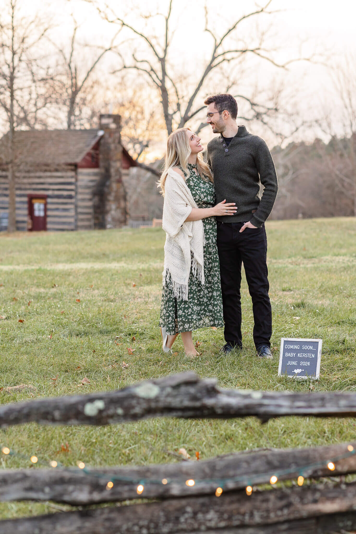 A mom and dad to be embracing in front of a sign announcing their baby.
