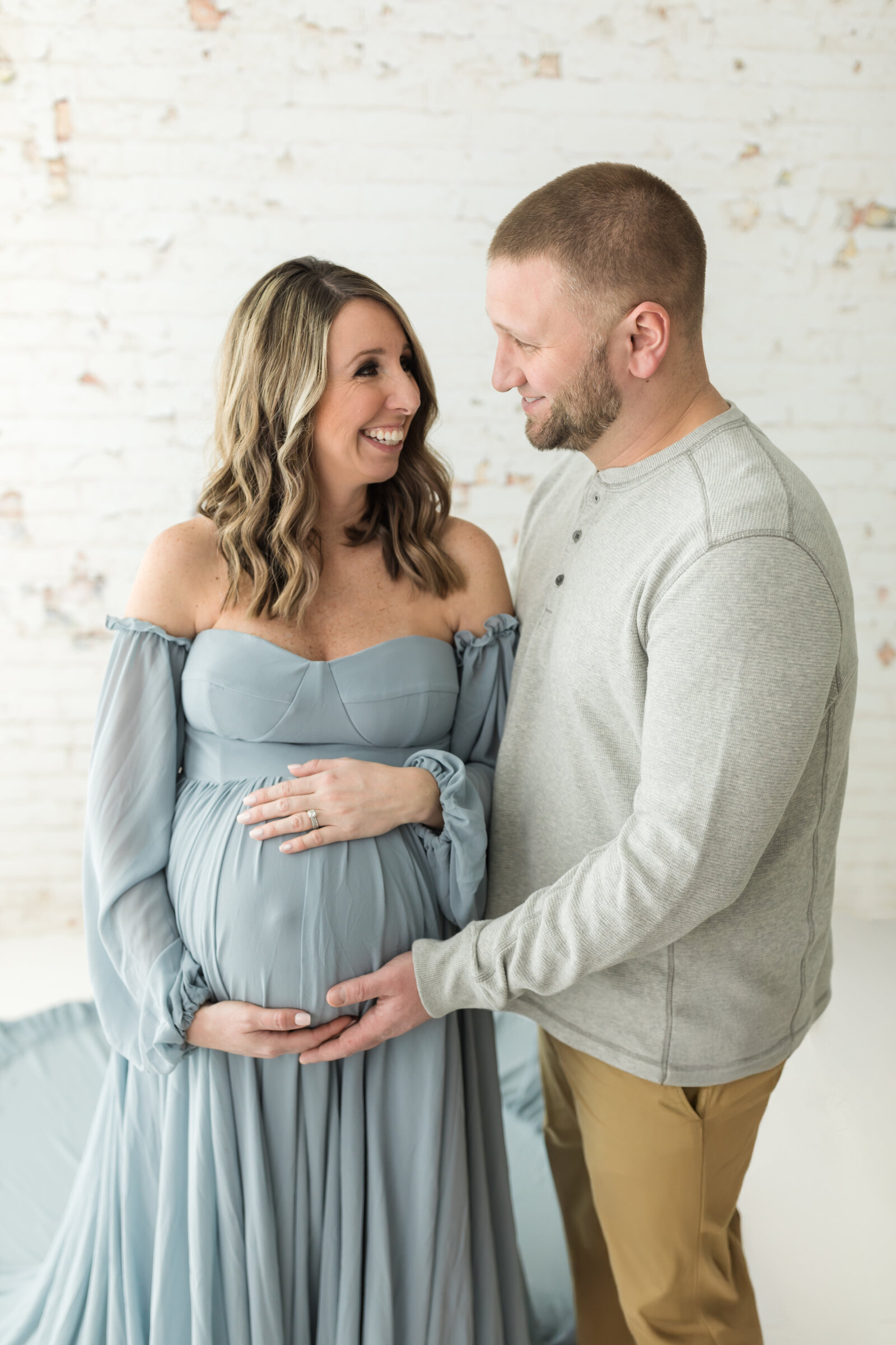 husband and pregnant wife in blue maternity gown holding baby bump for studio maternity photoshoot