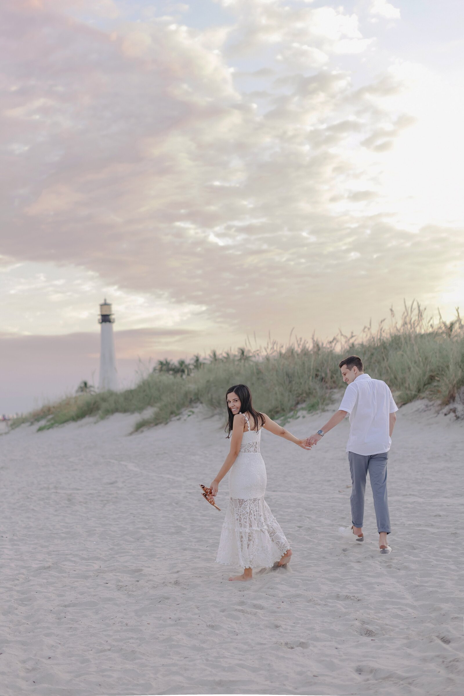 Couple walk hand in hand towards lighthouse on beach in Miami.