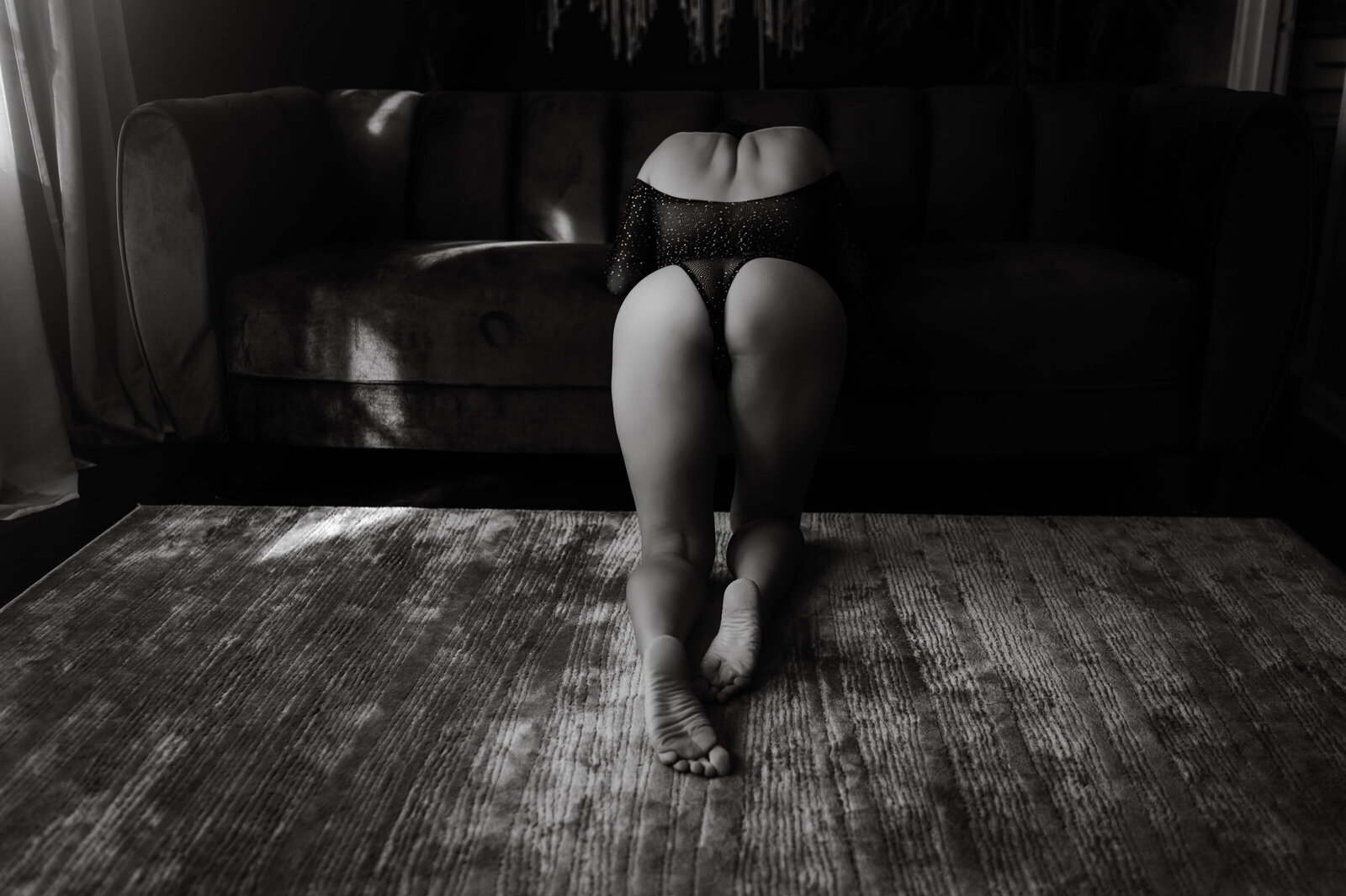 An image from Boudoir Photography in Memphis of a woman kneeling on the floor and leaning on a couch in mesh lingerie